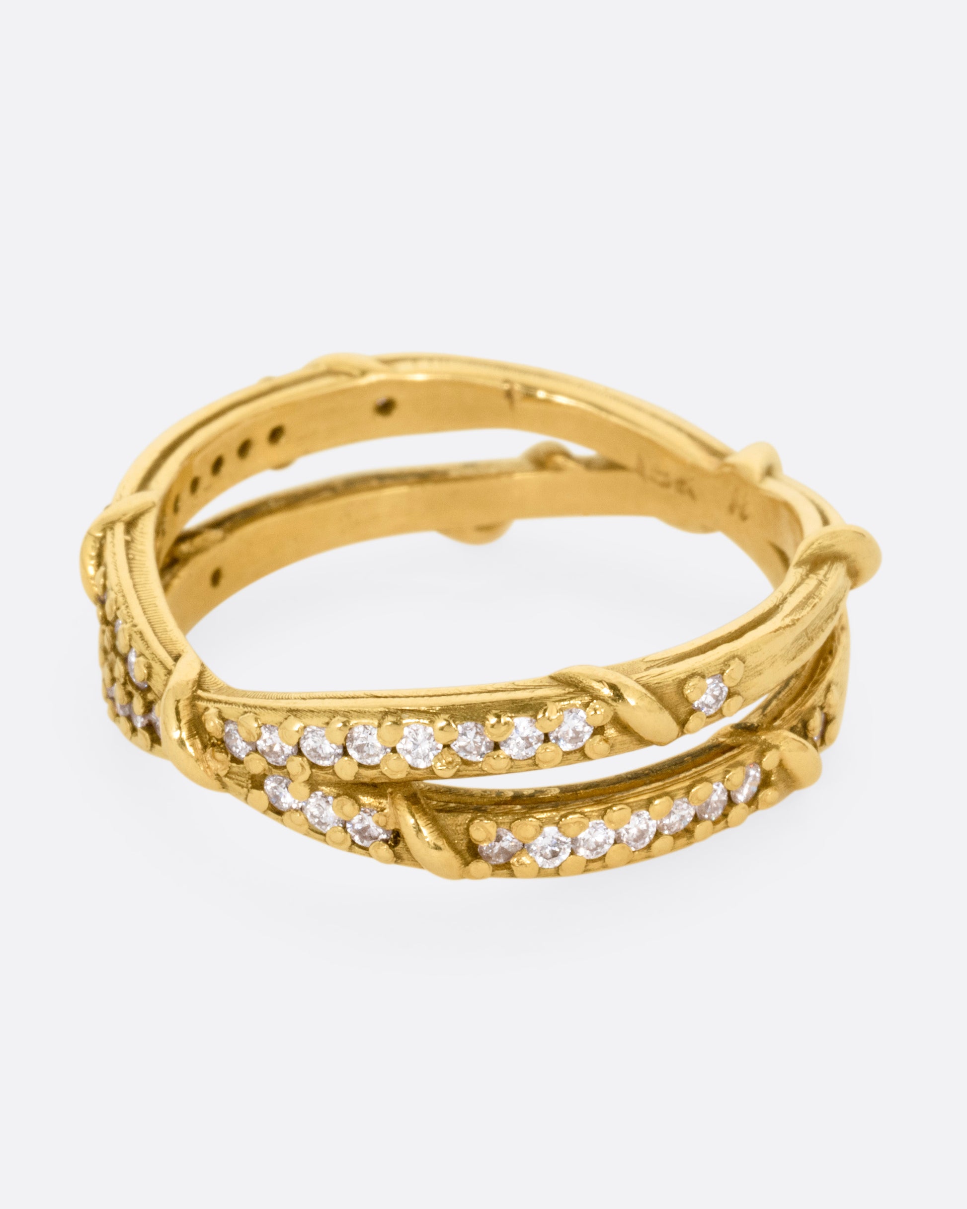 A yellow gold ring with two eternity bands intersecting at the middle and wrapped in vines and colorless diamonds. Shown from the side.