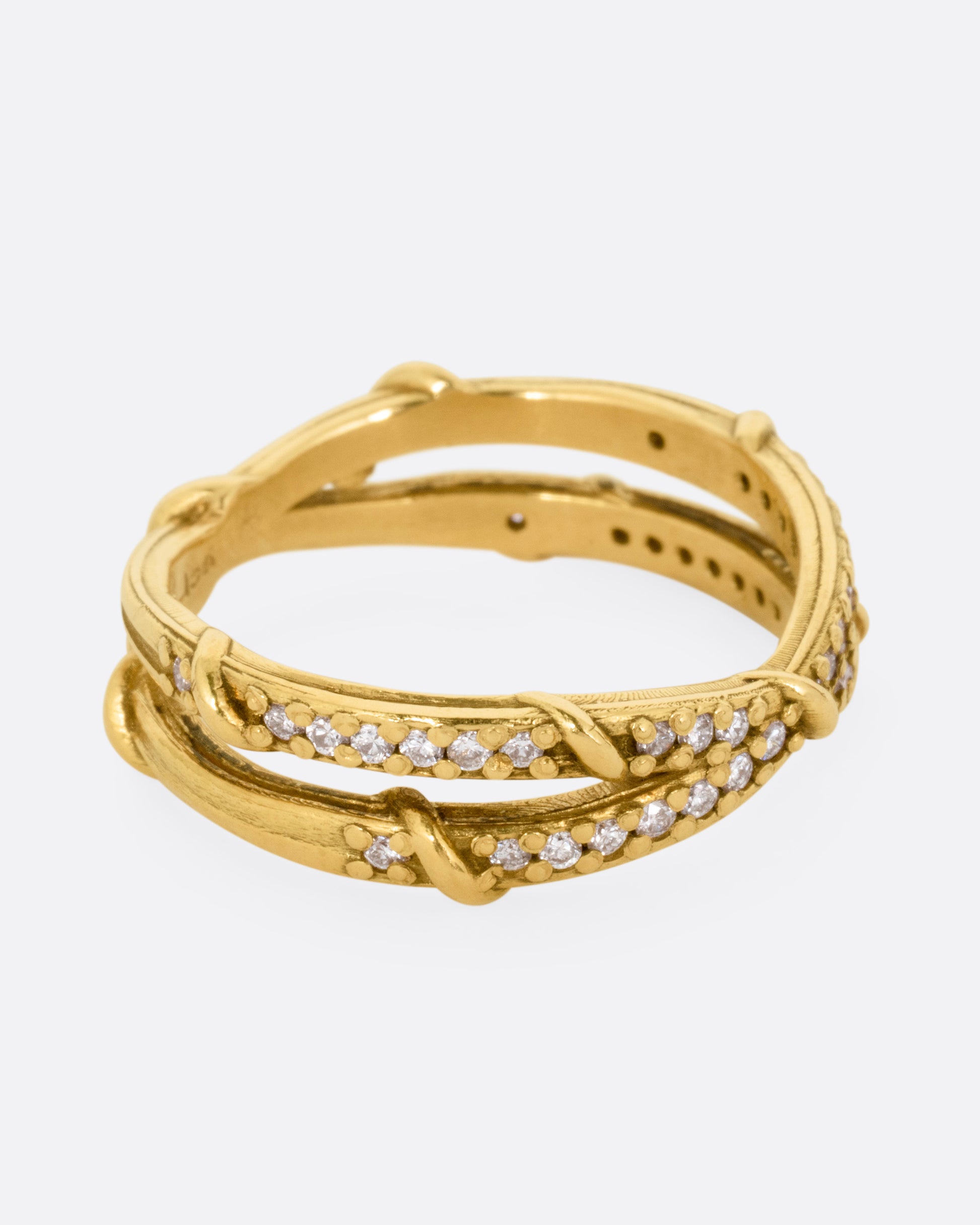 A yellow gold ring with two eternity bands intersecting at the middle and wrapped in vines and colorless diamonds. Shown from the side.