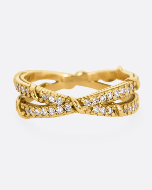 A yellow gold ring with two eternity bands intersecting at the middle and wrapped in vines and colorless diamonds. Shown from the front.