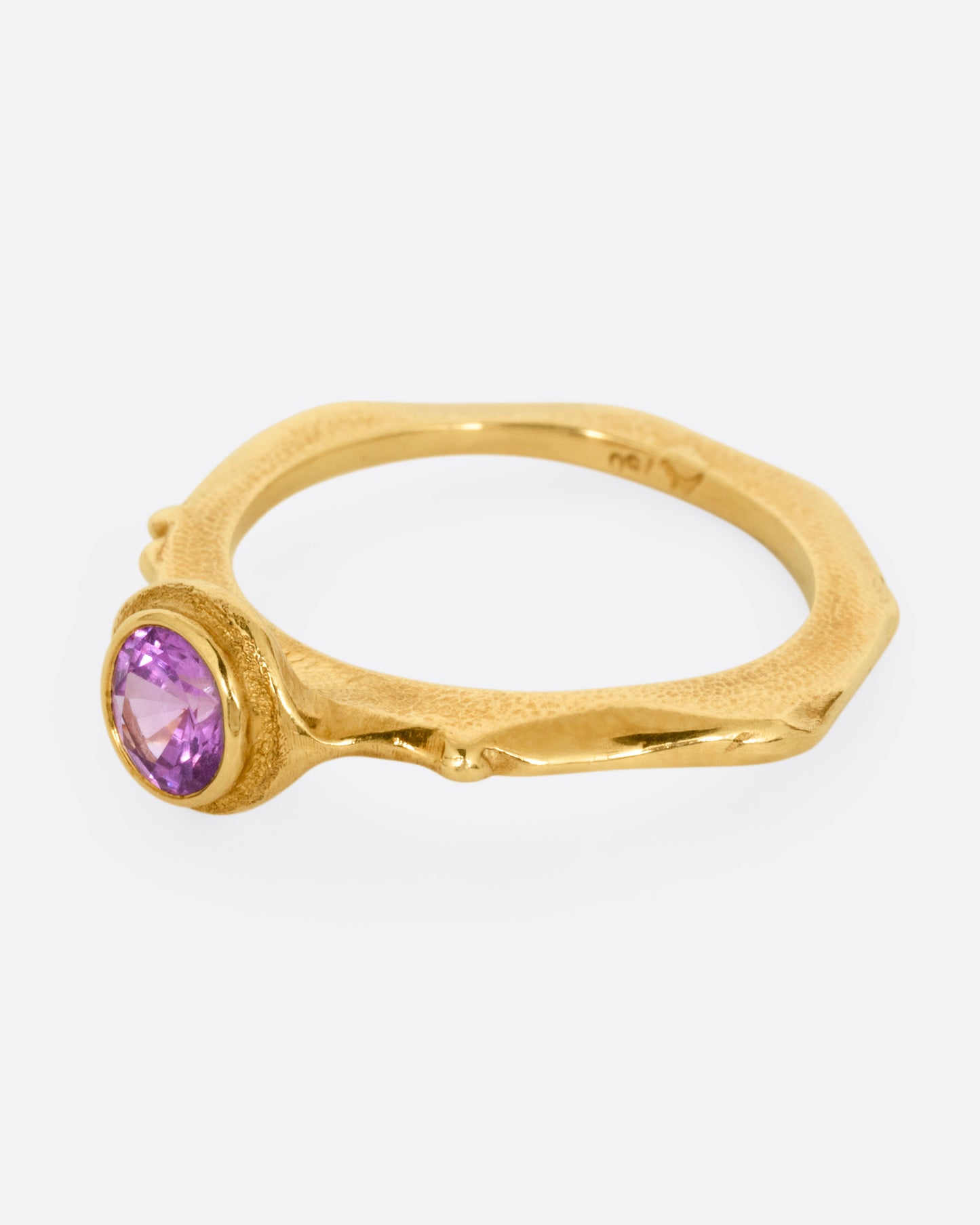 A yellow gold narrow sculptural ring with a purple sapphire, shown from the side.