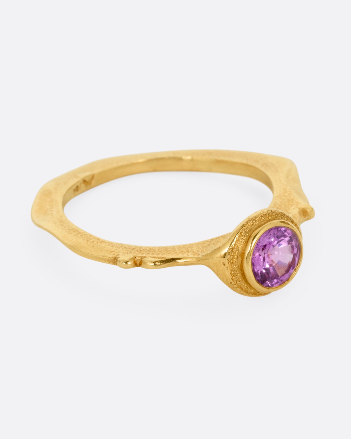 A yellow gold narrow sculptural ring with a purple sapphire, shown from the side.