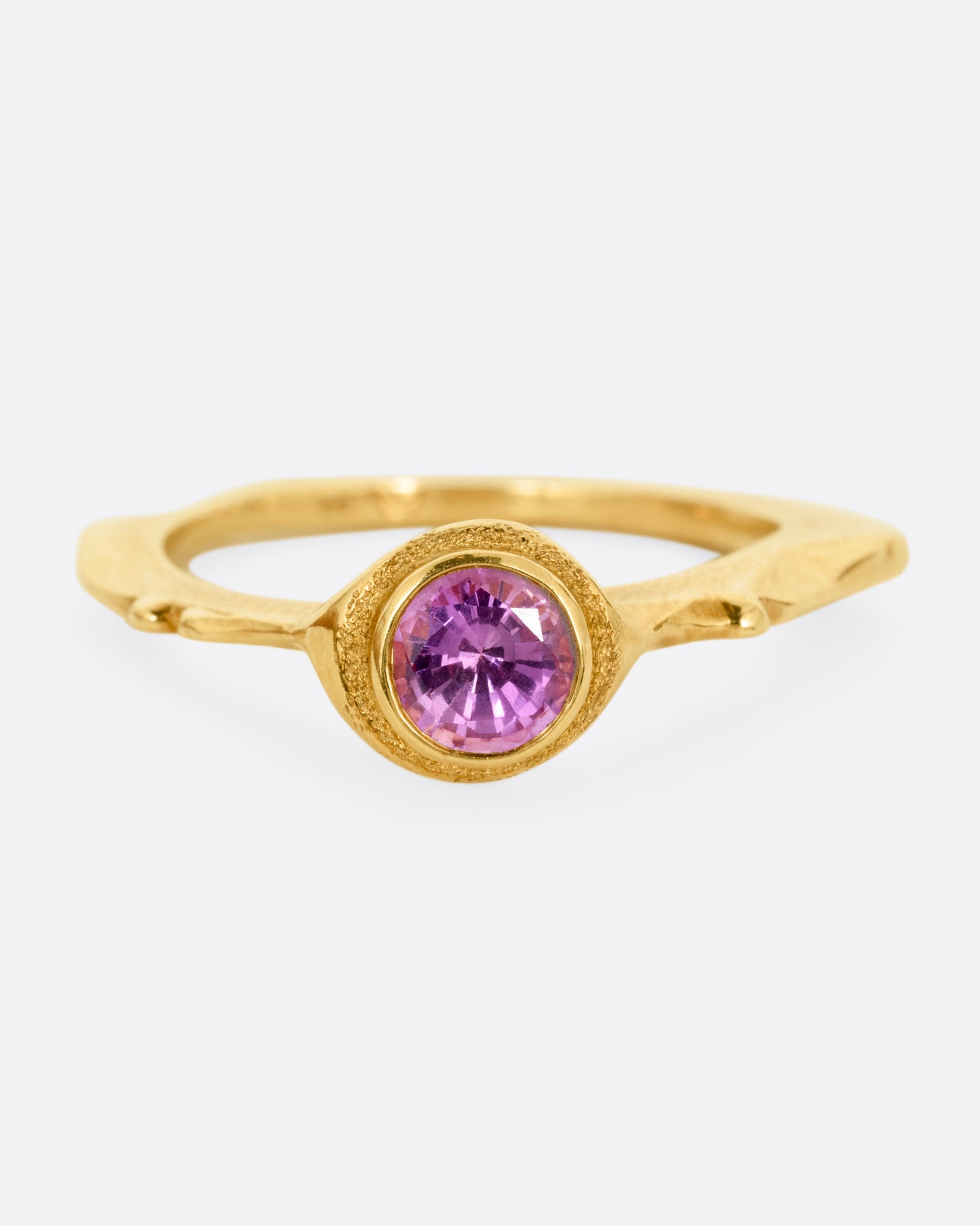 A yellow gold narrow sculptural ring with a purple sapphire, shown from the front.