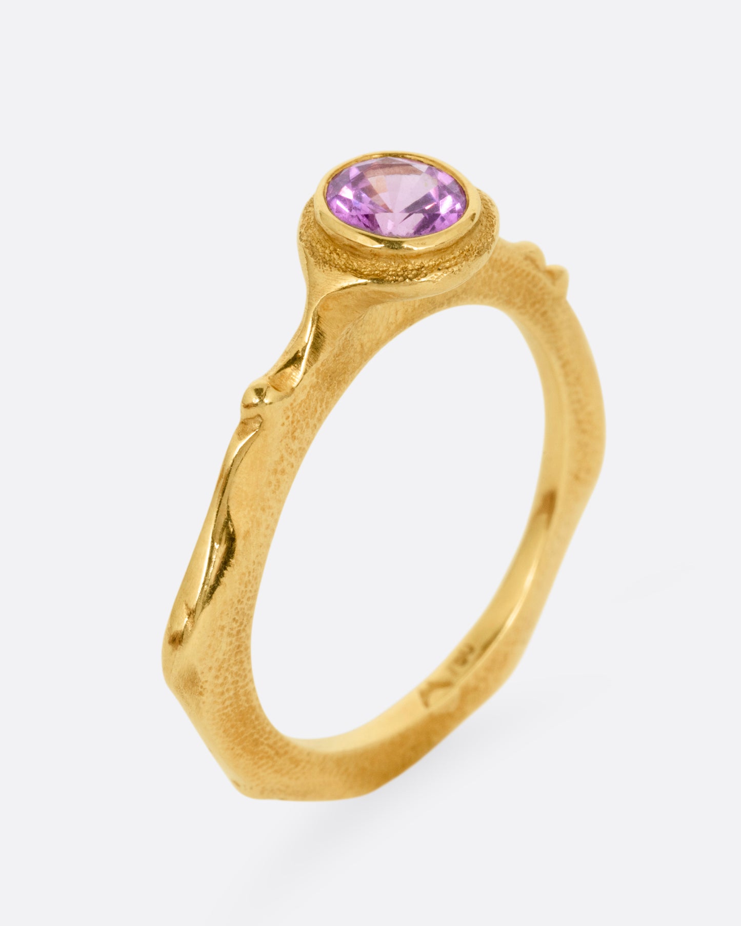 A yellow gold narrow sculptural ring with a purple sapphire, shown from the side standing up.
