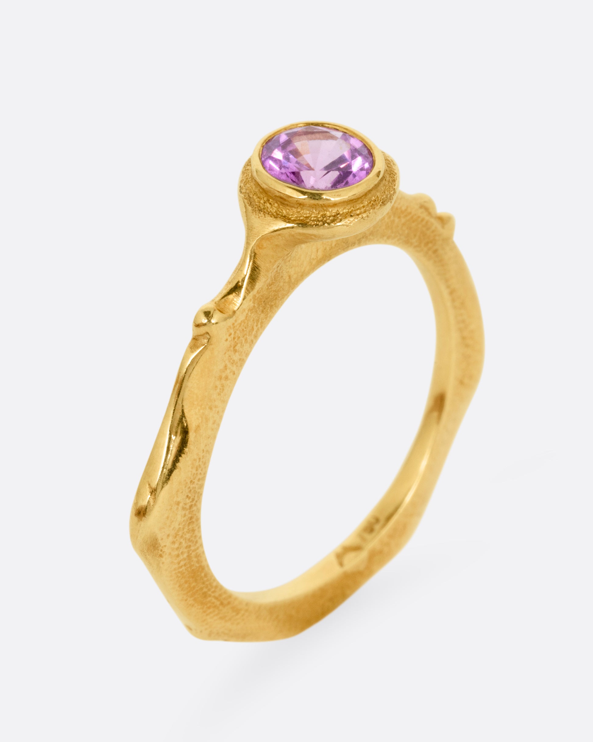 A yellow gold narrow sculptural ring with a purple sapphire, shown from the side standing up.