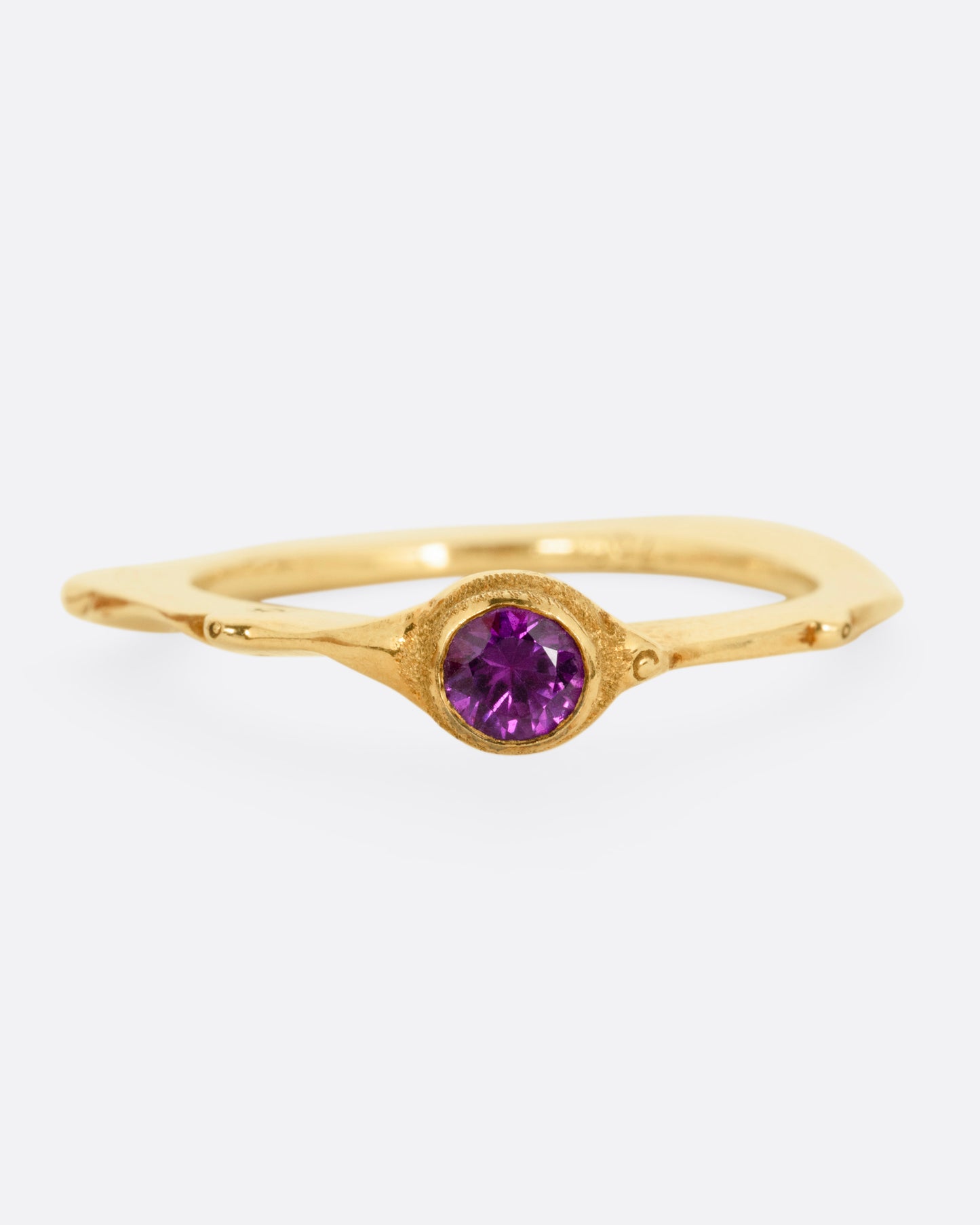 A yellow gold narrow sculptural ring with a purple sapphire, shown from the front.