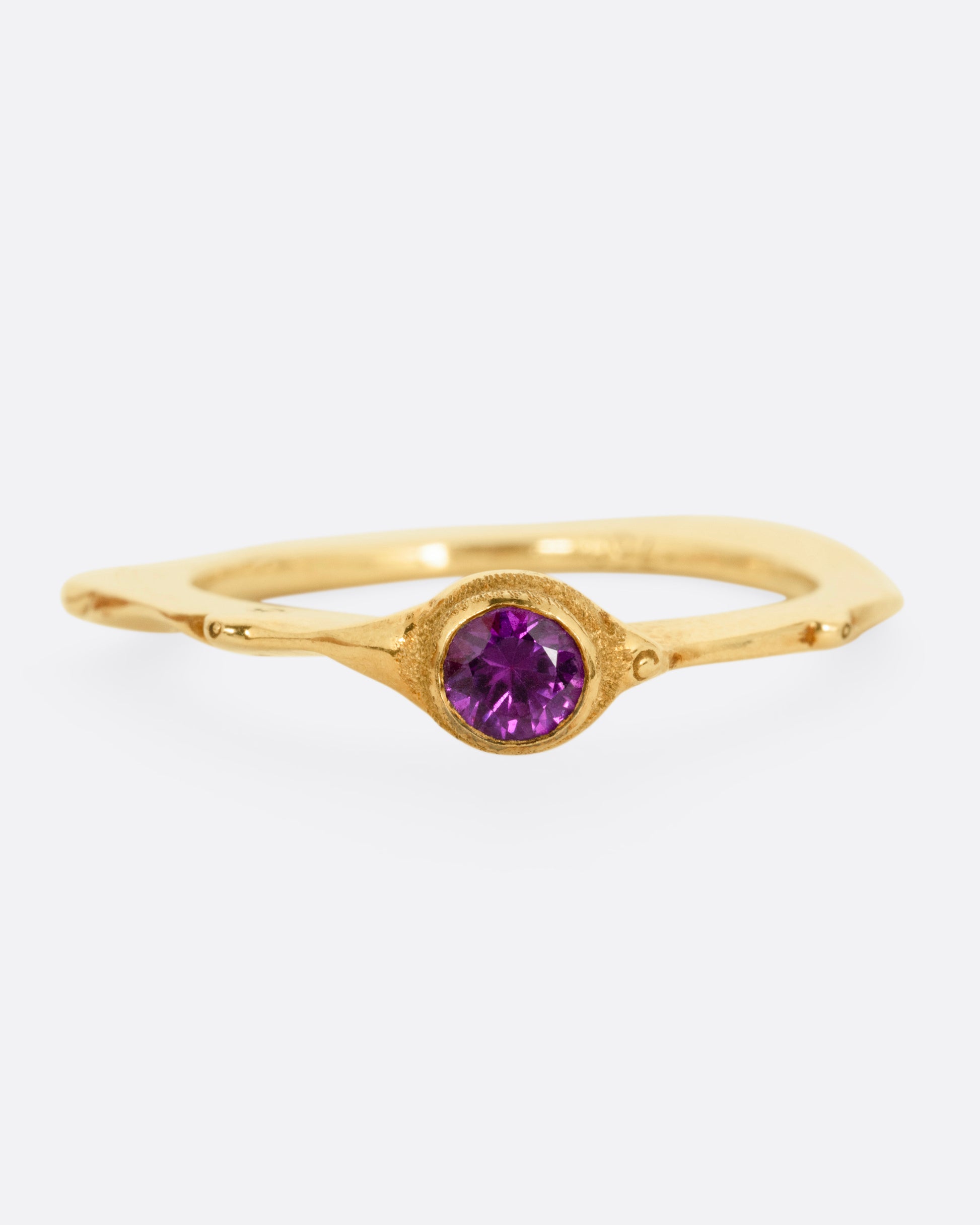 A yellow gold narrow sculptural ring with a purple sapphire, shown from the front.