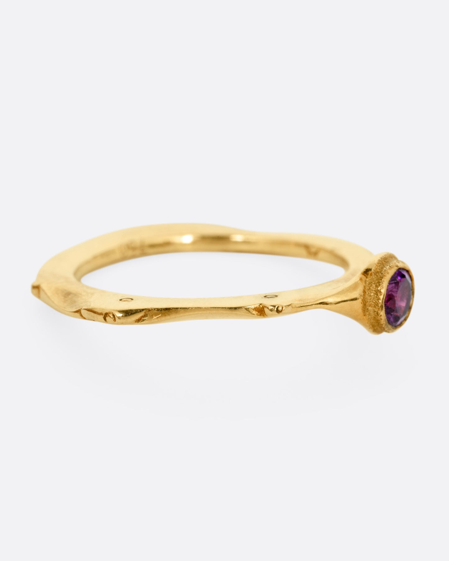 A yellow gold narrow sculptural ring with a purple sapphire, shown from the side.