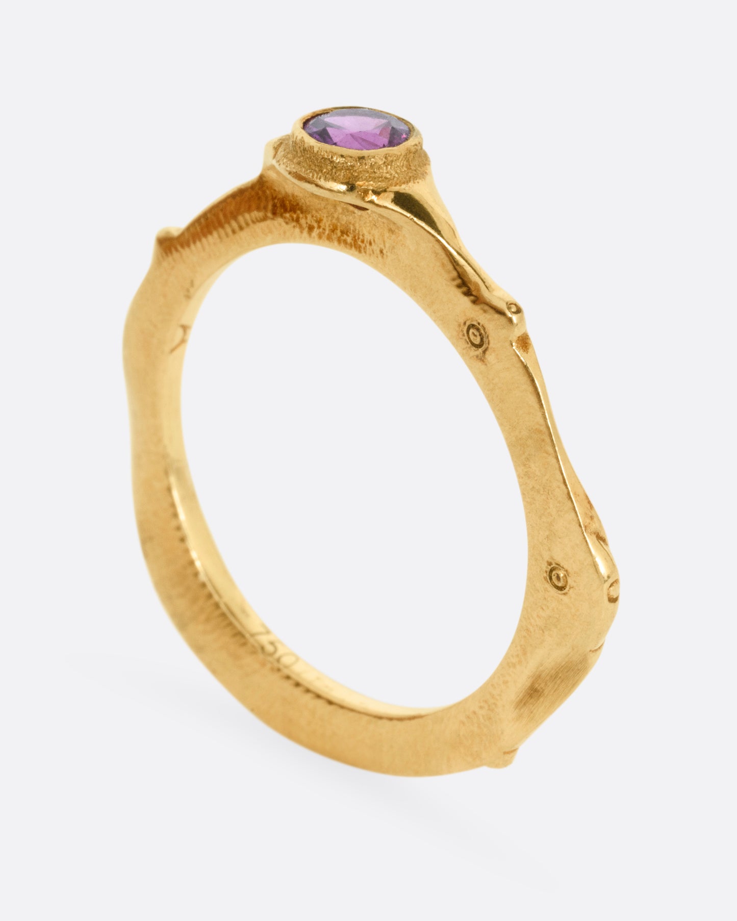A yellow gold narrow sculptural ring with a purple sapphire, shown from the side standing up.