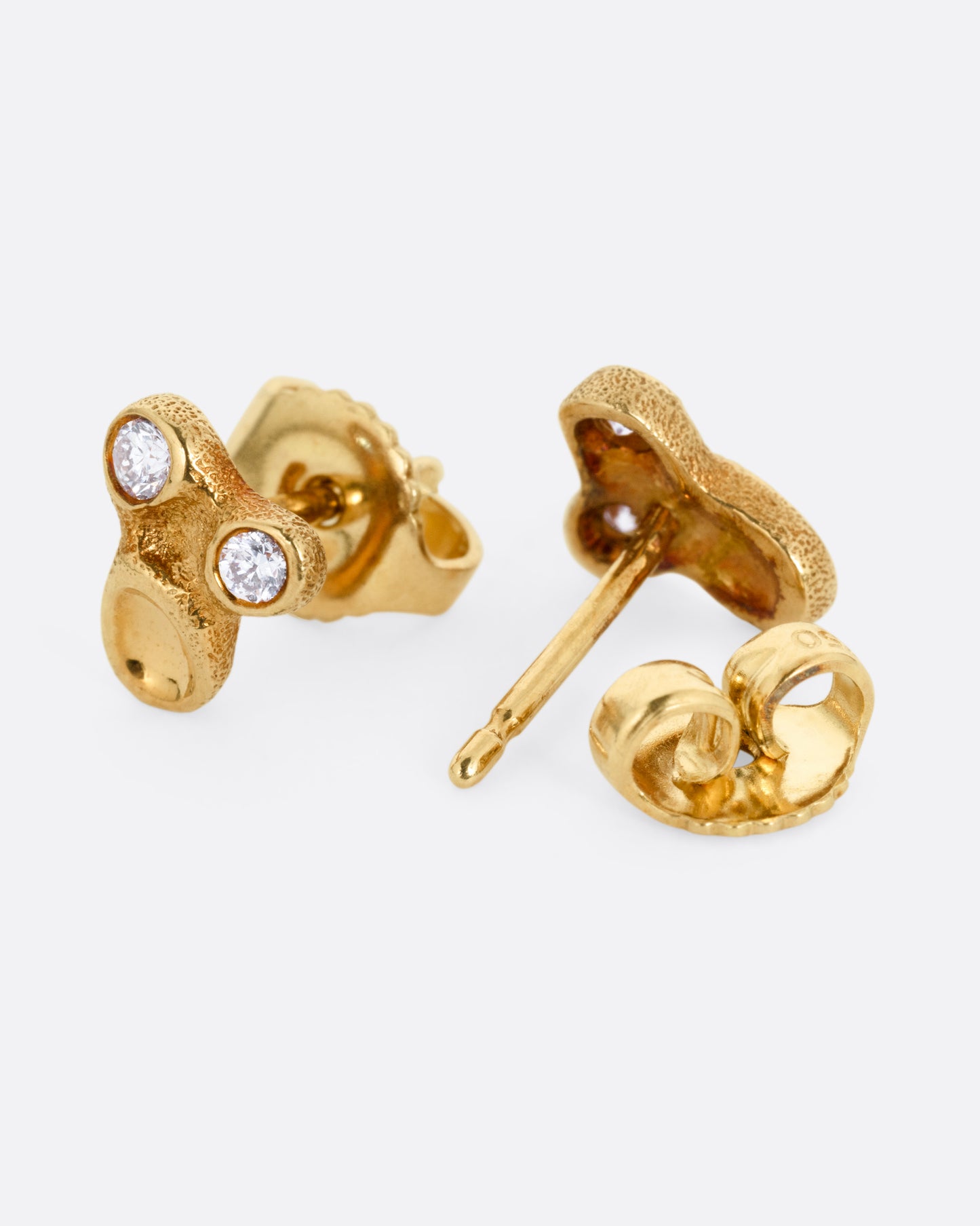 A pair of yellow gold stud earrings with two bezel set diamonds and smooth depressions. One earring is shown from the front, the other open from the back.