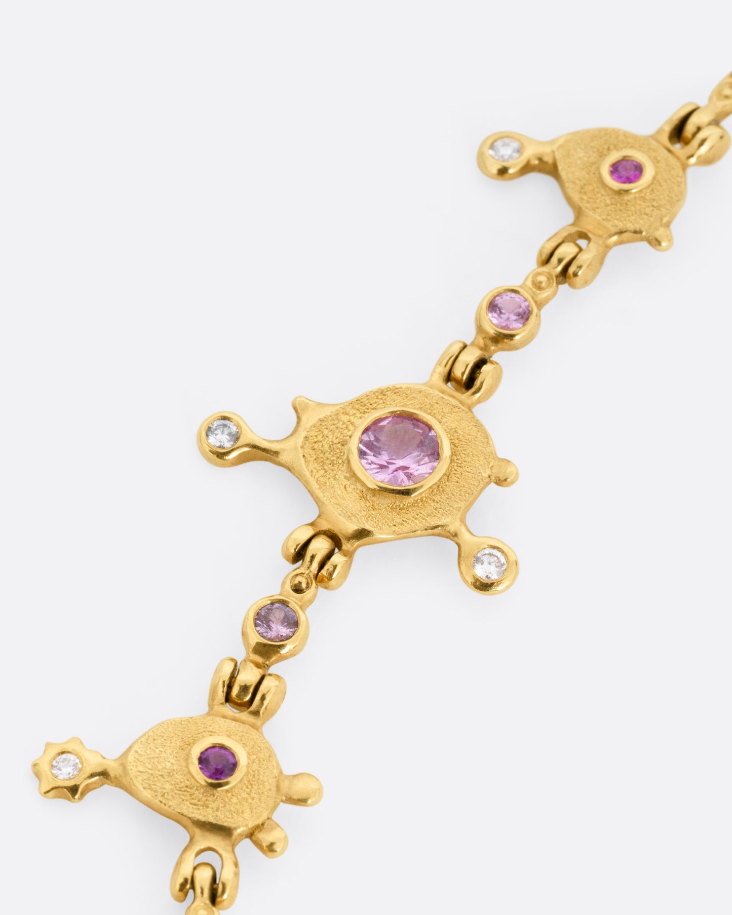 A close up of a yellow gold necklace with purple sapphires and diamonds set in handmade stations, shown lying flat.