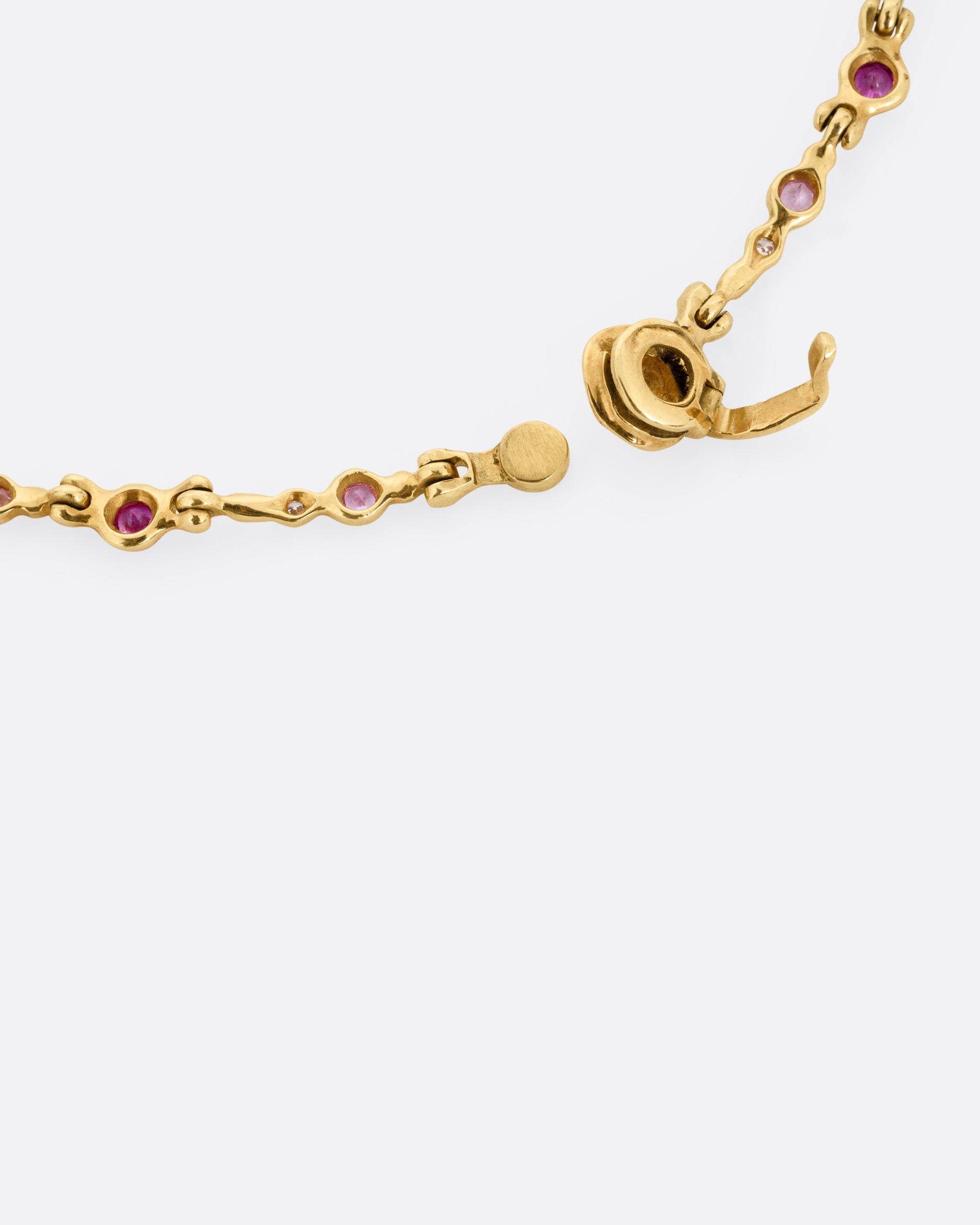 A close up  of the clasp of a yellow gold necklace with purple sapphires and diamonds set in handmade stations.