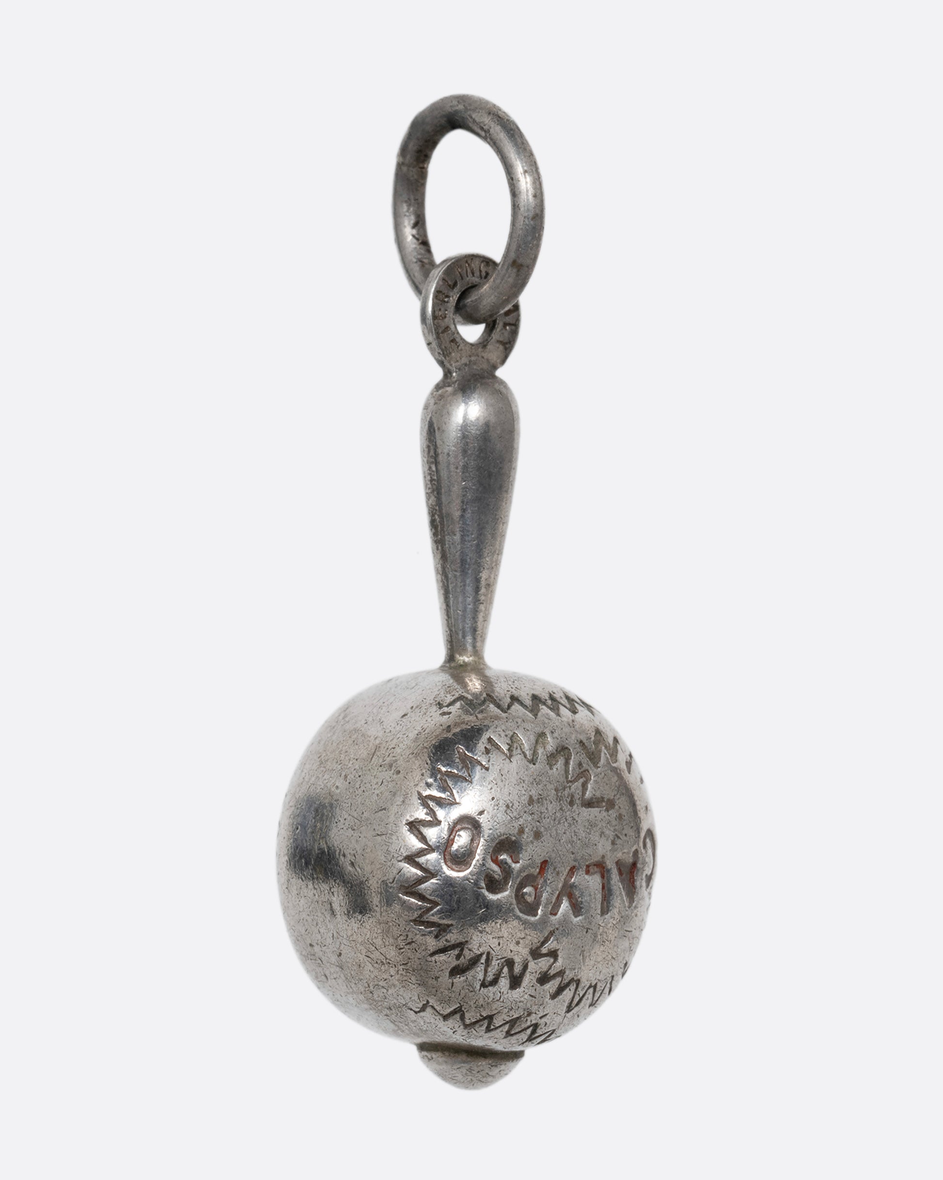 A silver maraca charm with 'Calypso' engraved on it. Shown from the side.