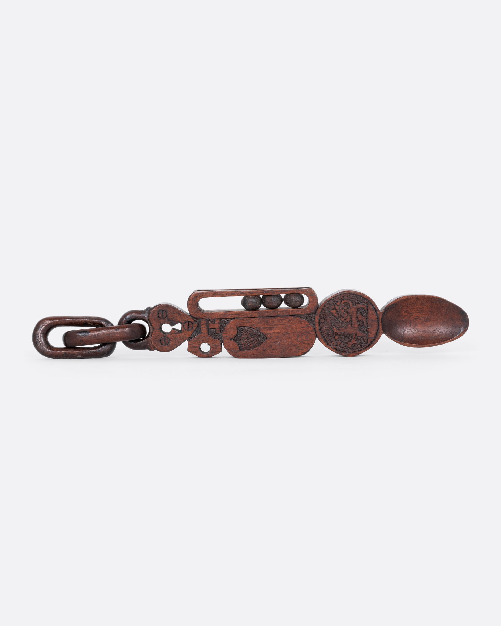 A wooden whimsy spoon hand carved from a single piece of wood. A padlocked heart with chain links, a shield, gryphon emblem, and three moving balls are all carved on its handle. Shown from the side.