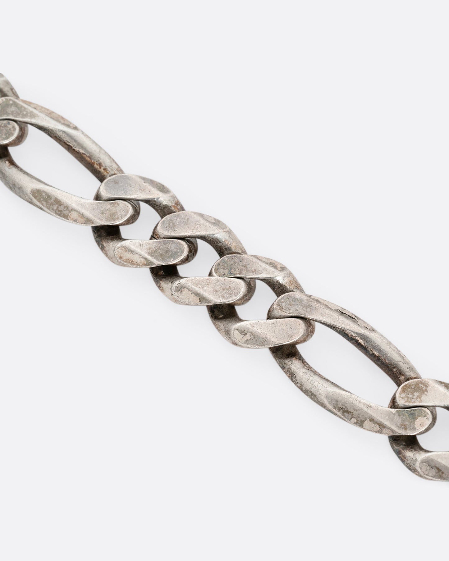 A close up of a wide silver figaro chain bracelet. 