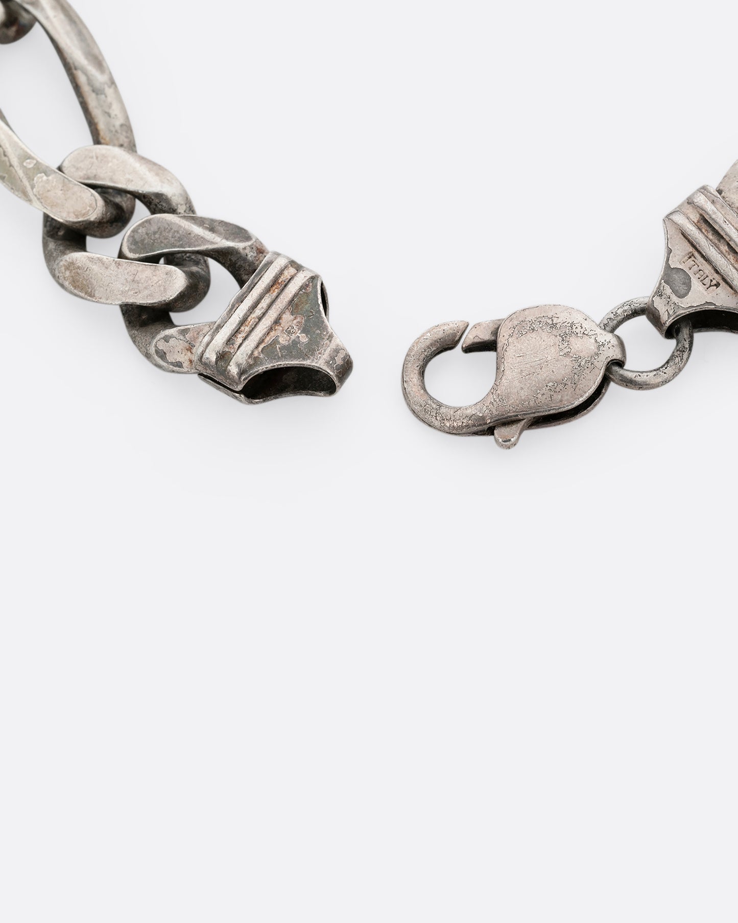 A close up of the lobster clasp of a wide silver figaro chain bracelet. Shown from the top.