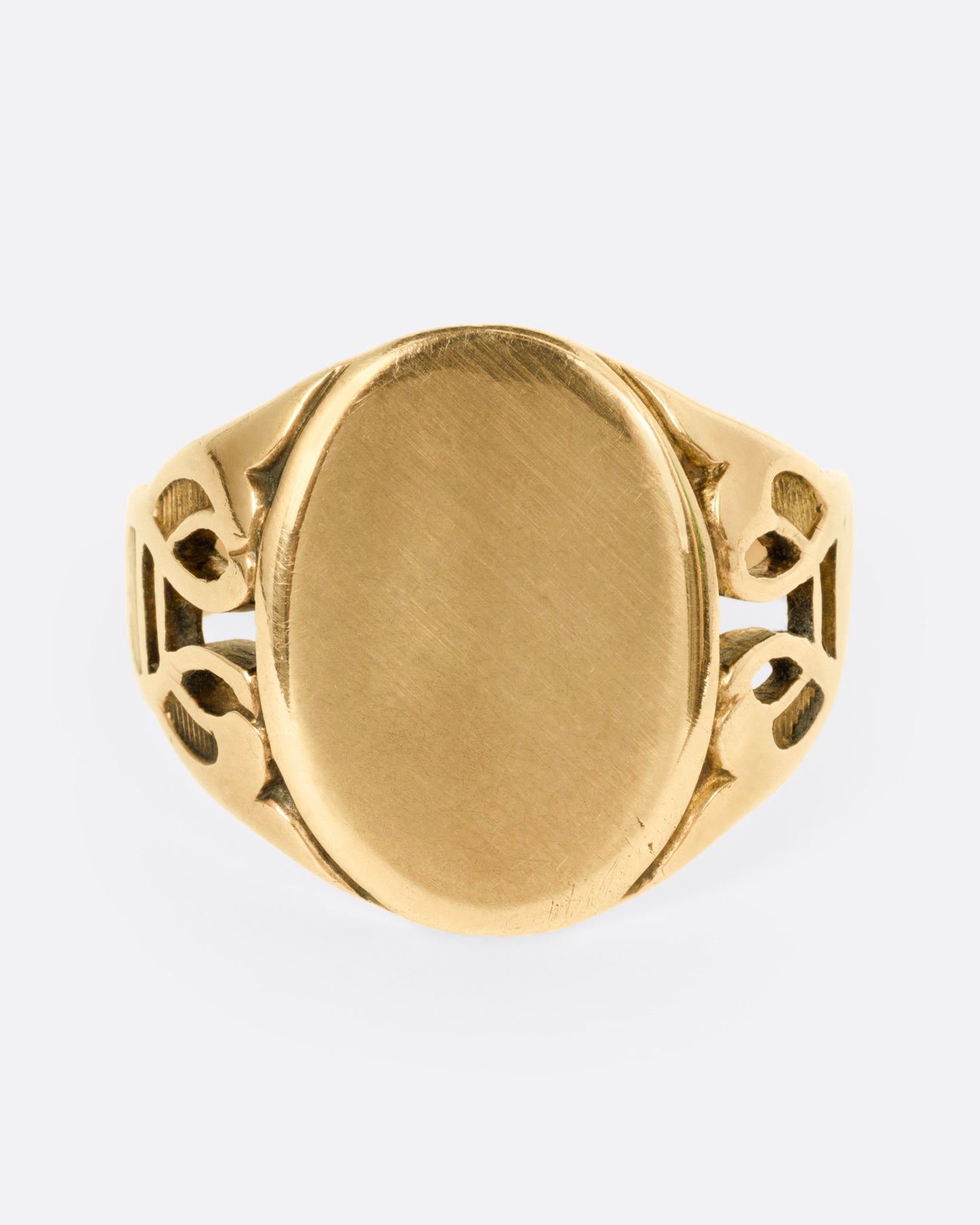 A yellow gold ring with an oval face and an ornate band, shown from the front.