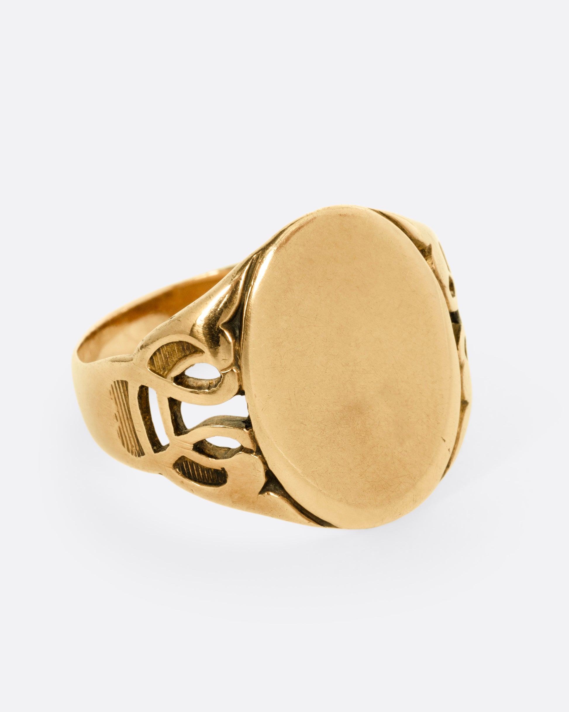 A yellow gold ring with an oval face and an ornate band, shown from the side.