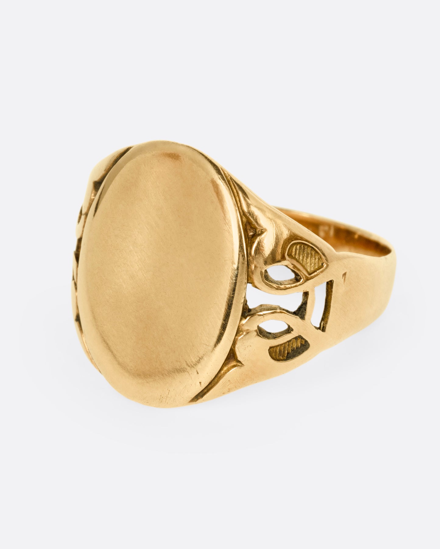 A yellow gold ring with an oval face and an ornate band, shown from the side.