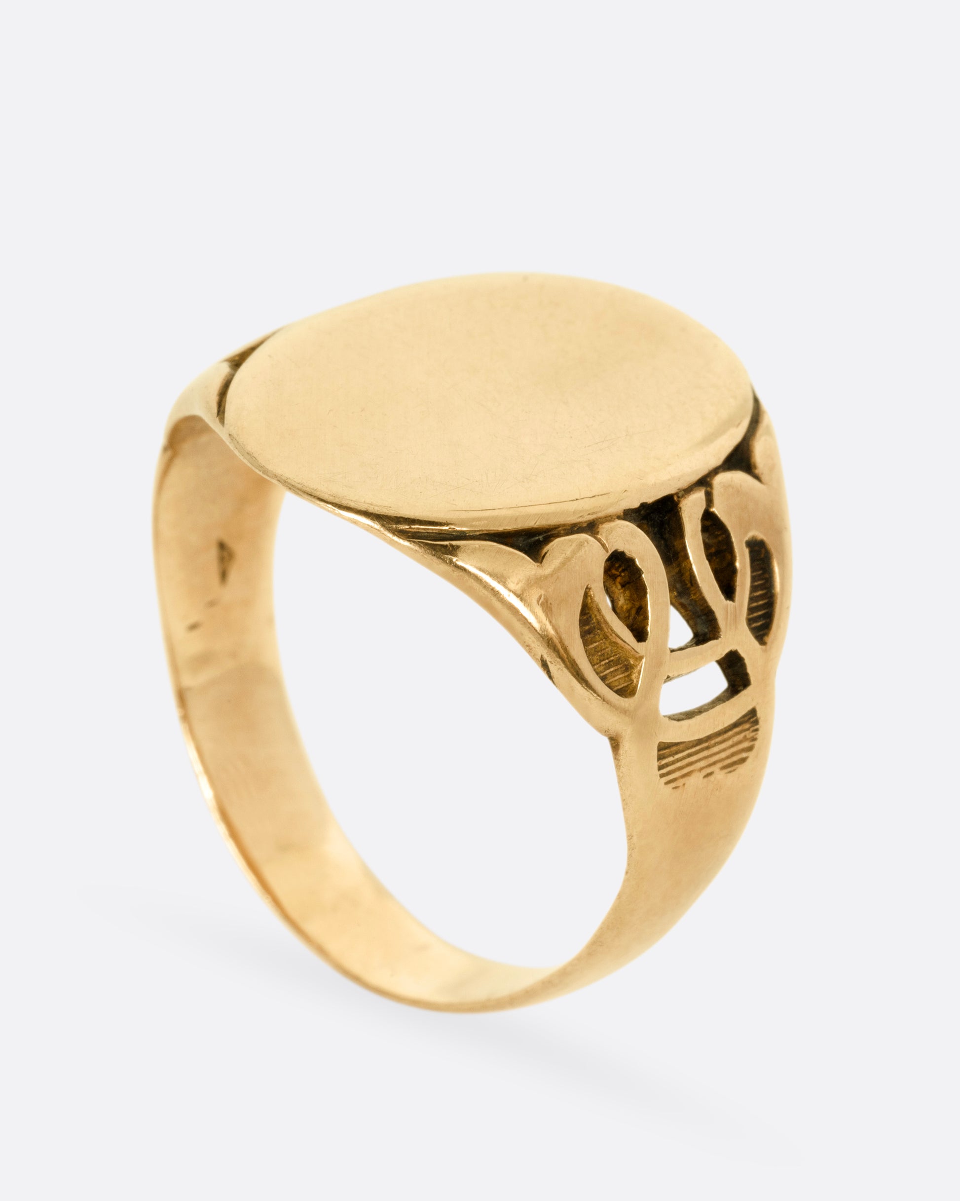 A yellow gold ring with an oval face and an ornate band, shown from the side standing up.