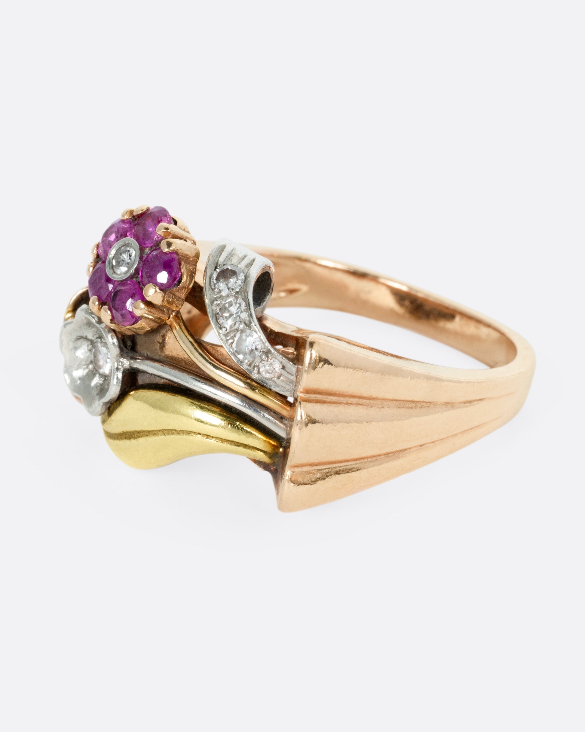 A yellow, white, and rose gold ring with ruby and diamond flowers and diamond details, shown from the side.
