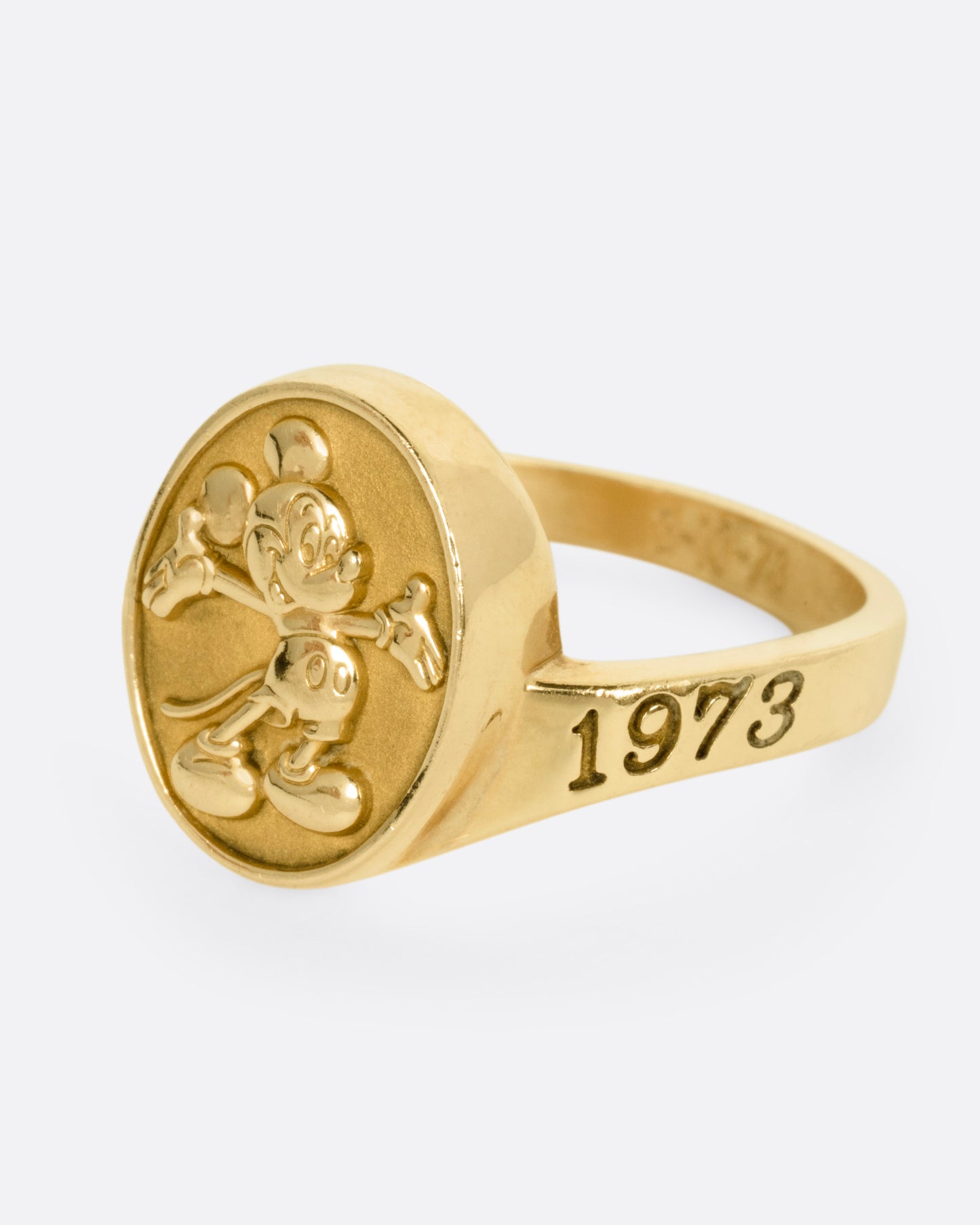 A yellow gold ring with Mickey Mouse on its face and '1973' on its shoulder, shown from the side.