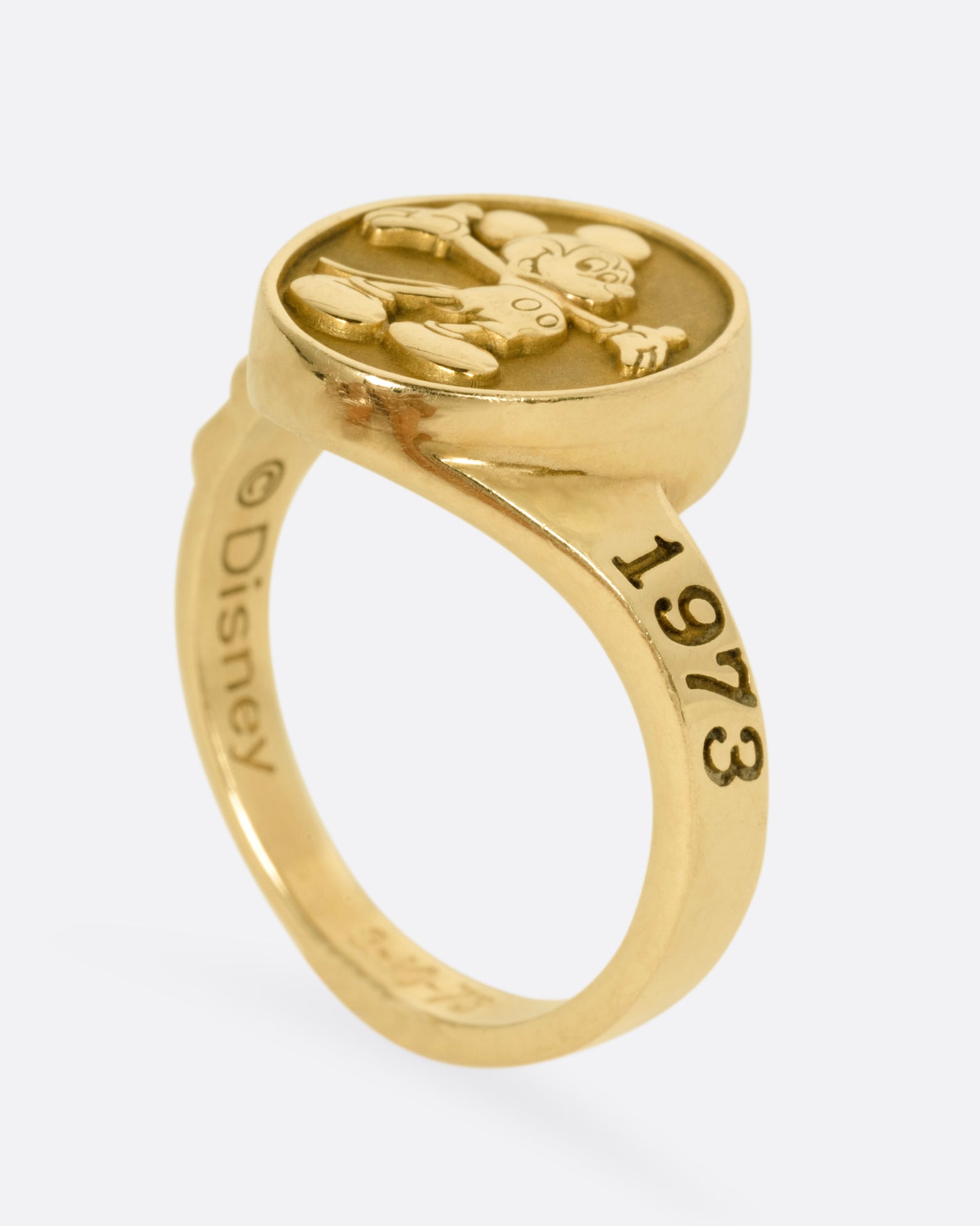 A yellow gold ring with Mickey Mouse on its face and '1973' on its shoulder, shown standing up from the side.