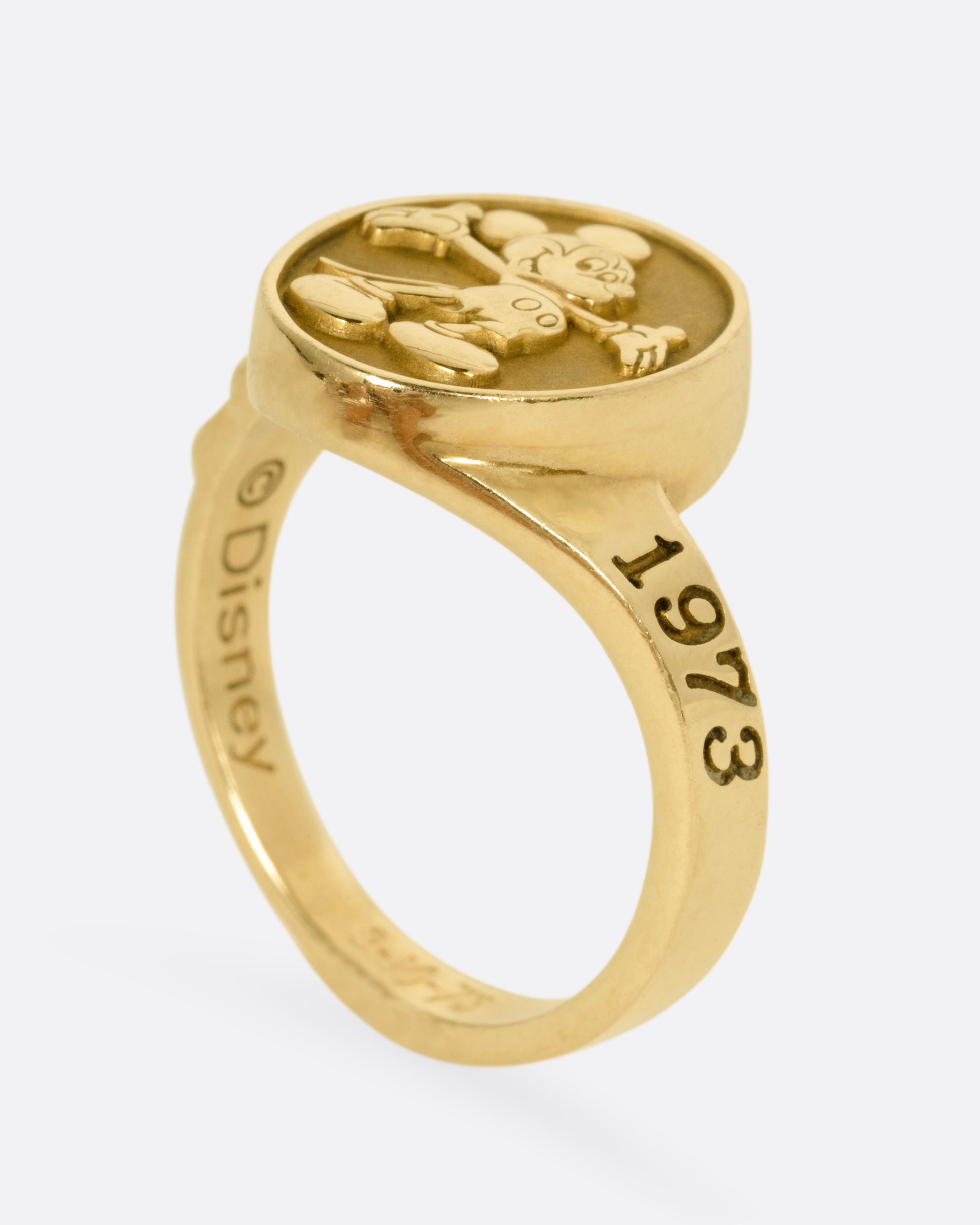 A yellow gold ring with Mickey Mouse on its face and '1973' on its shoulder, shown standing up from the side.