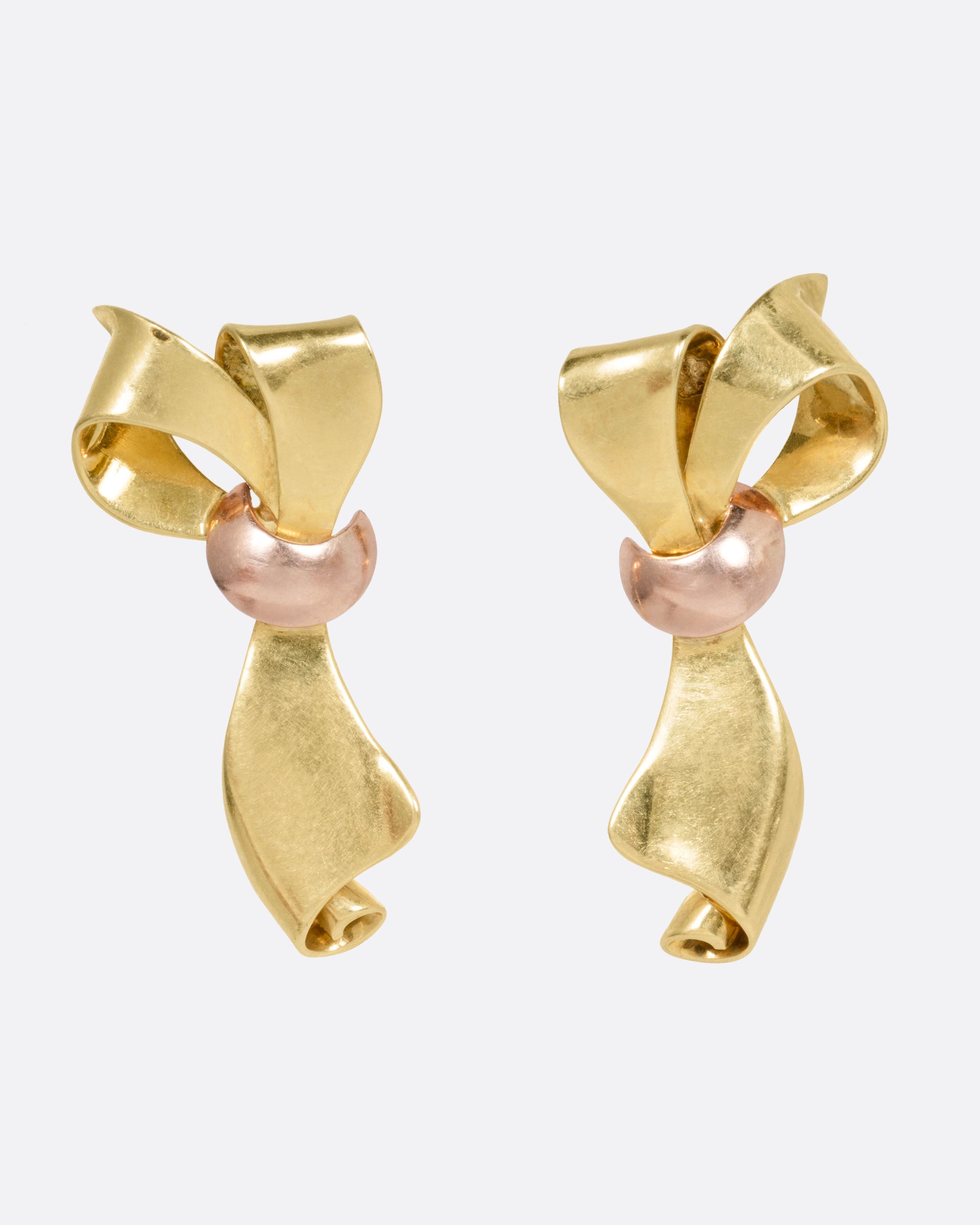 A pair of yellow gold ribbon shaped earrings with a rose gold knot, shown from the front.