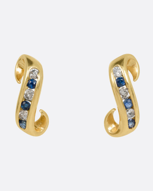 A pair of yellow gold scroll shaped earrings with a queue of channel set diamonds and sapphires, shown from the front.
