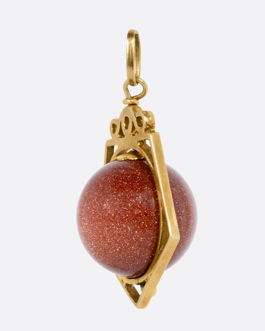 A yellow gold pendant with a spinning Italian goldstone sphere, shown from the side.