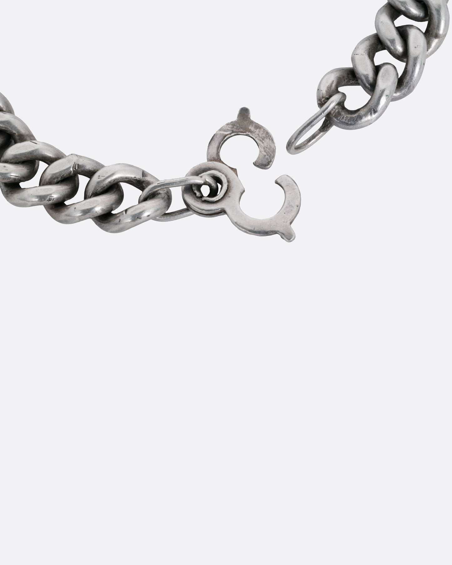A close up of the clasp of a silver curb chain ID bracelet, shown open.