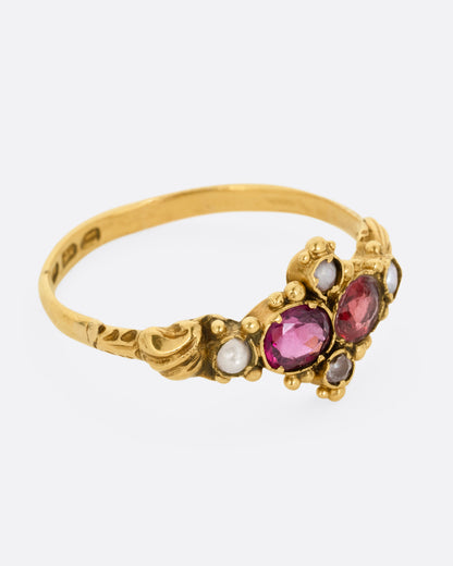 A yellow gold ring with garnets and seed pearls. Shown from the side.