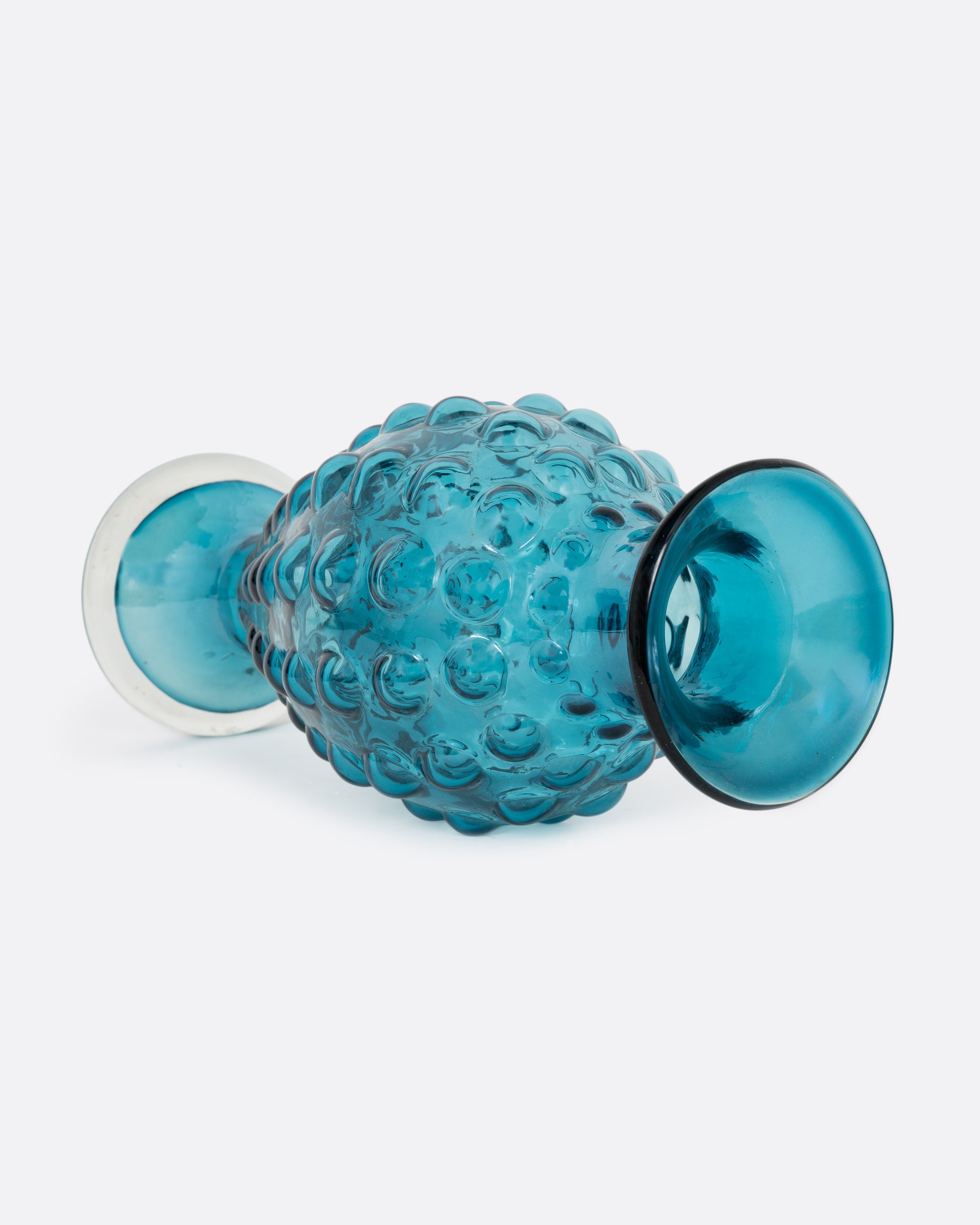 A teal hourglass glass vase with a bubbled texture. Shown lying on its side from the side.
