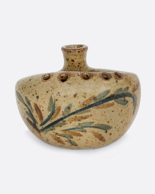 A ceramic bud vase with five small holes for flowers and a cleft at the front with a hand painted floral design. Shown from the front.