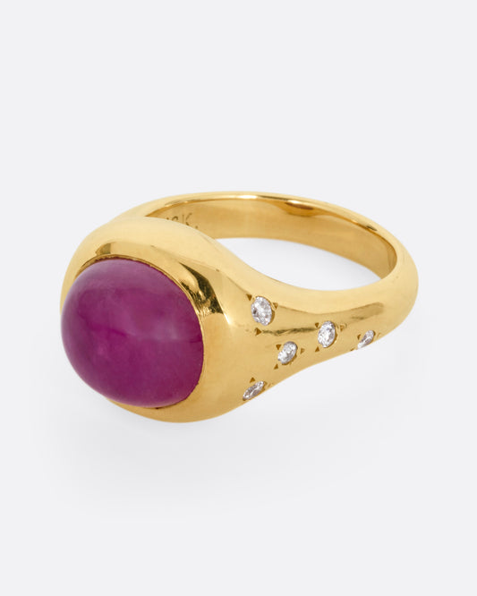 A yellow gold signet ring with a ruby cabochon and diamonds on either shoulder. Shown from the side at an angle.