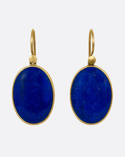 A pair of oval lapis earrings with yellow gold bezels and ear hooks. Shown from the front.