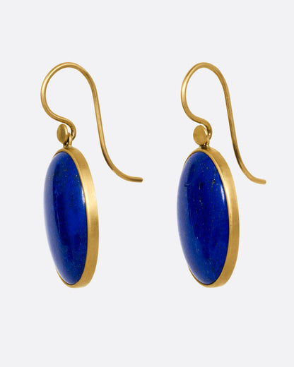 A pair of oval lapis earrings with yellow gold bezels and ear hooks. Shown from the side.