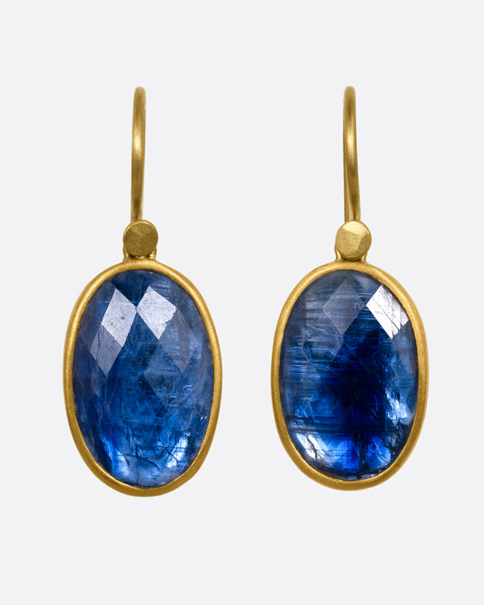 A pair of faceted blue kyanite earrings with yellow gold bezels and ear hooks. Shown from the front. 