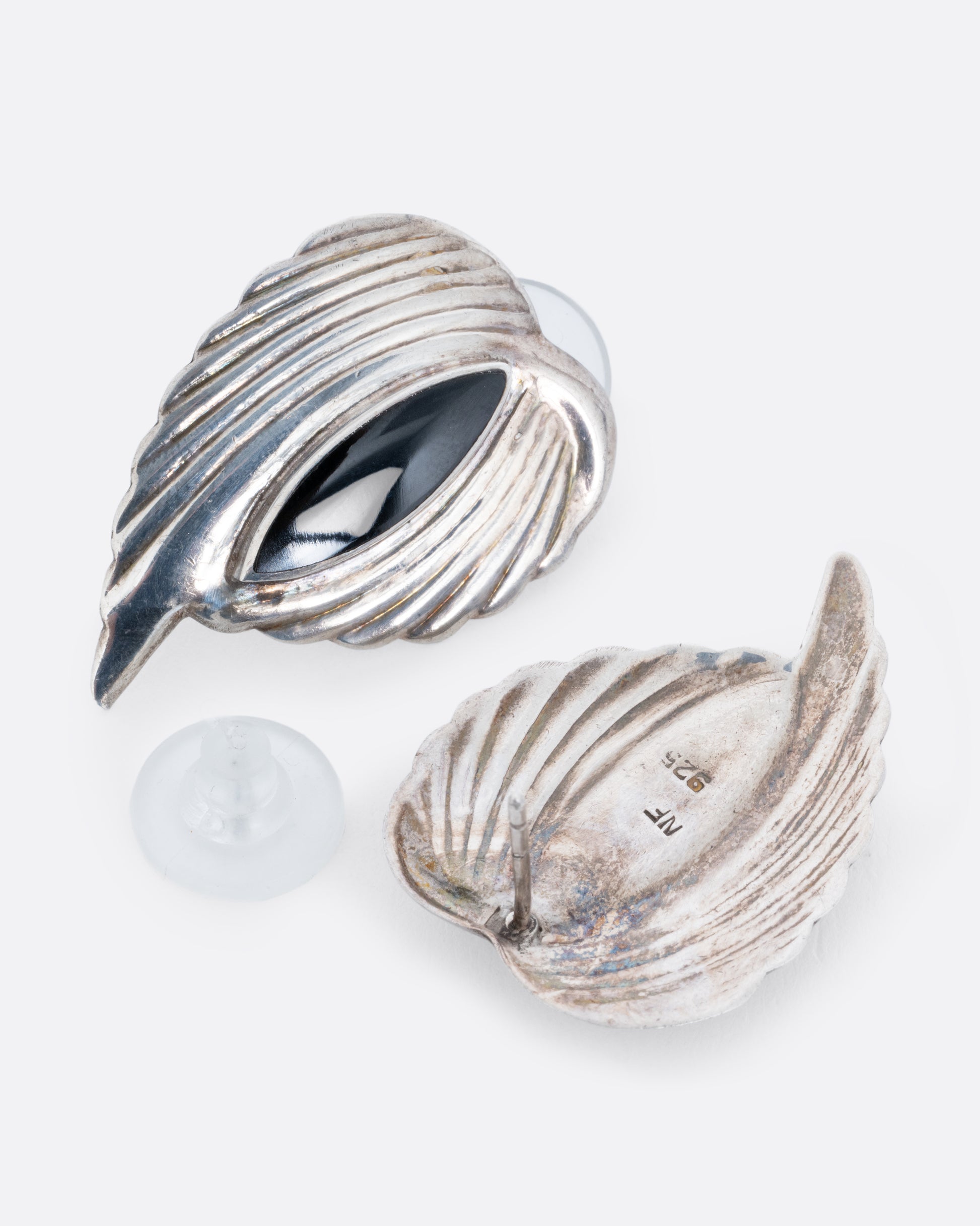 A pair of silver leaf stud earrings with bezel set marquis onyxes at the center. One earring is shown lying flat from the front. The other earring is shown open lying flat from the back.