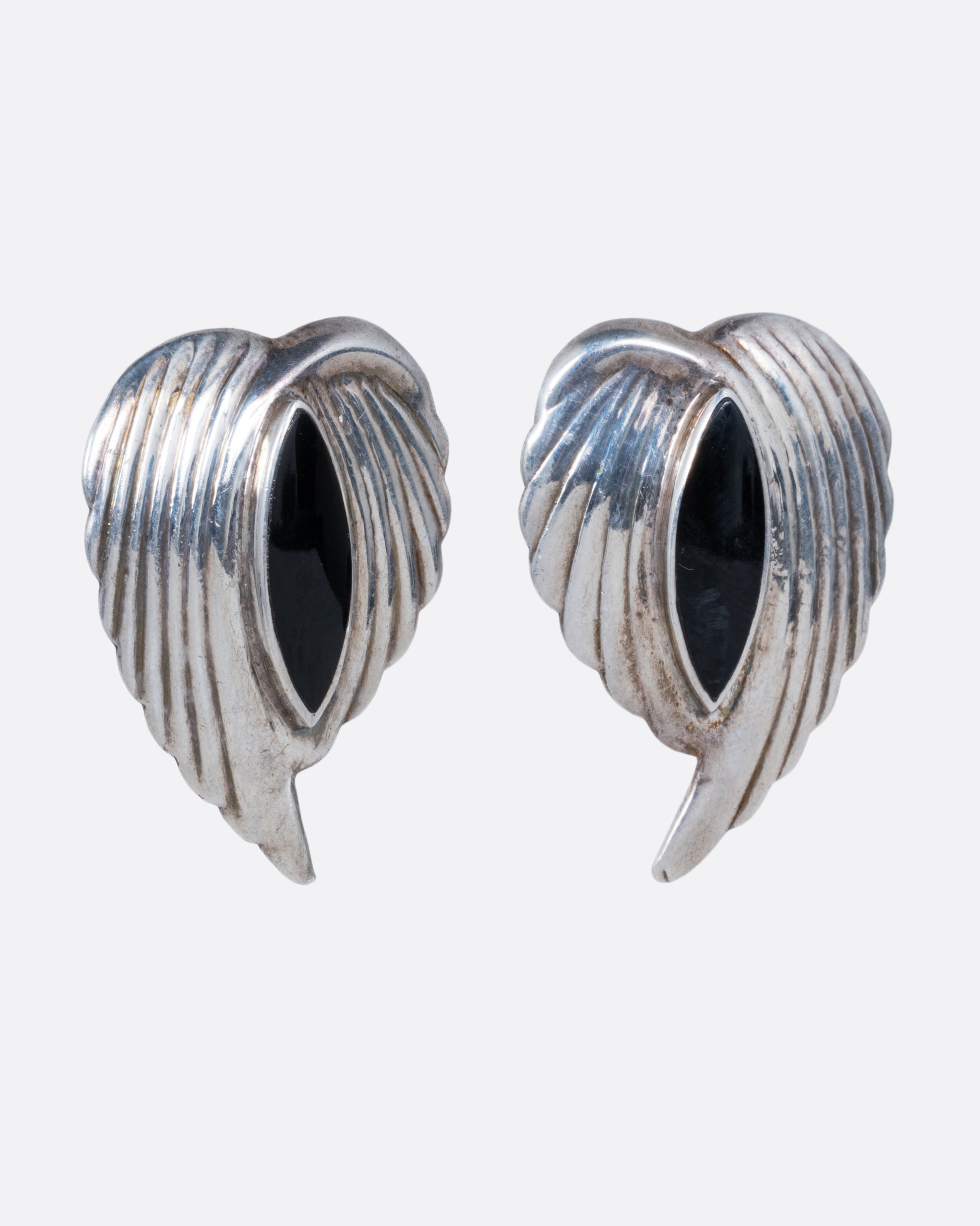 A pair of silver leaf stud earrings with bezel set marquis onyxes at the center. Shown from the side.