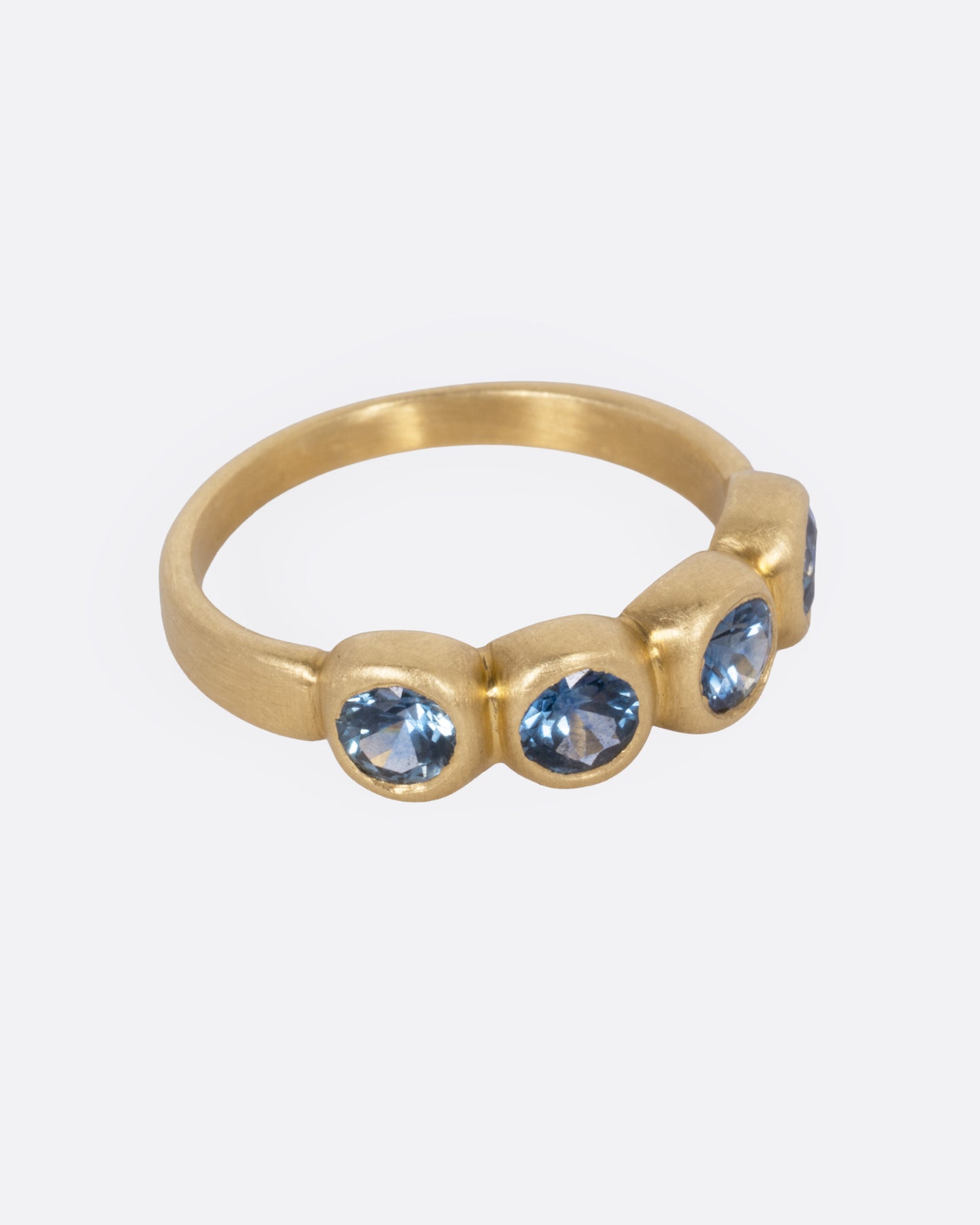 A yellow gold ring with four blue sapphires, shown from the side.
