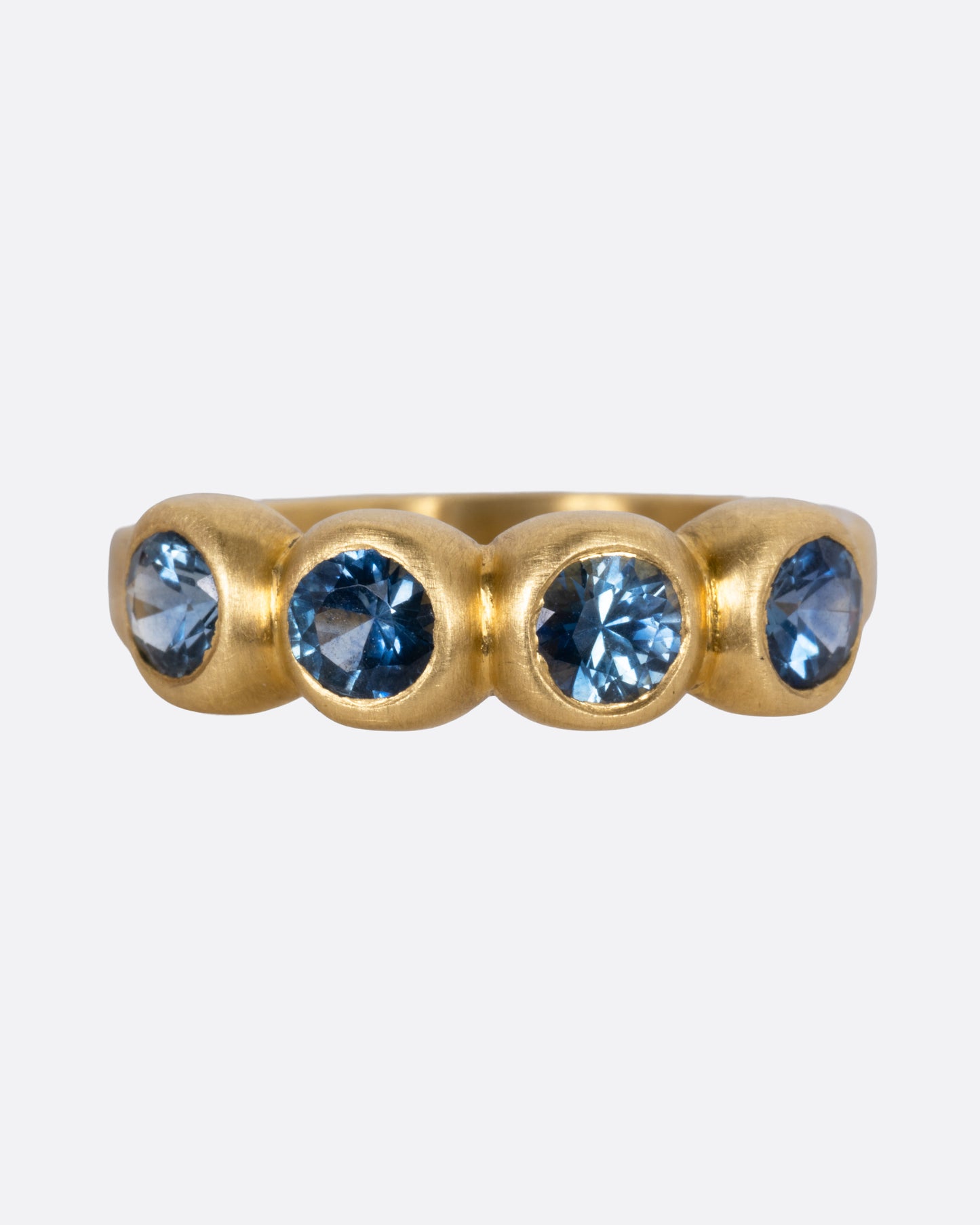 A yellow gold ring with four blue sapphires, shown from the front.