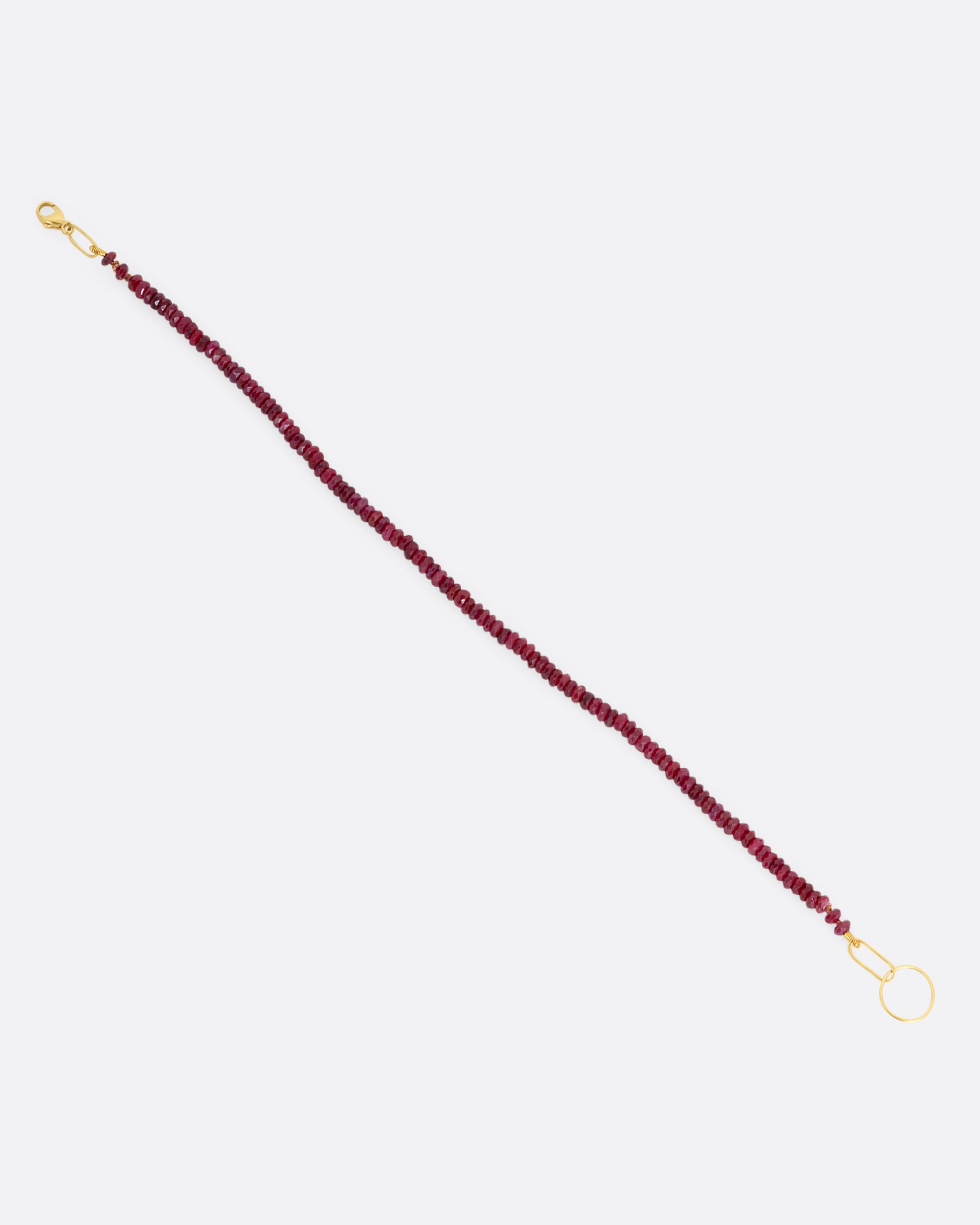 A beaded ruby bracelet with a yellow gold clasp. Shown open from the side.