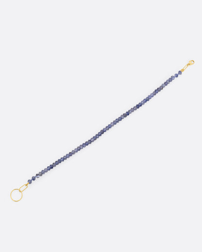 An iolite beaded bracelet with a yellow gold clasp. Shown open lying flat from the side.