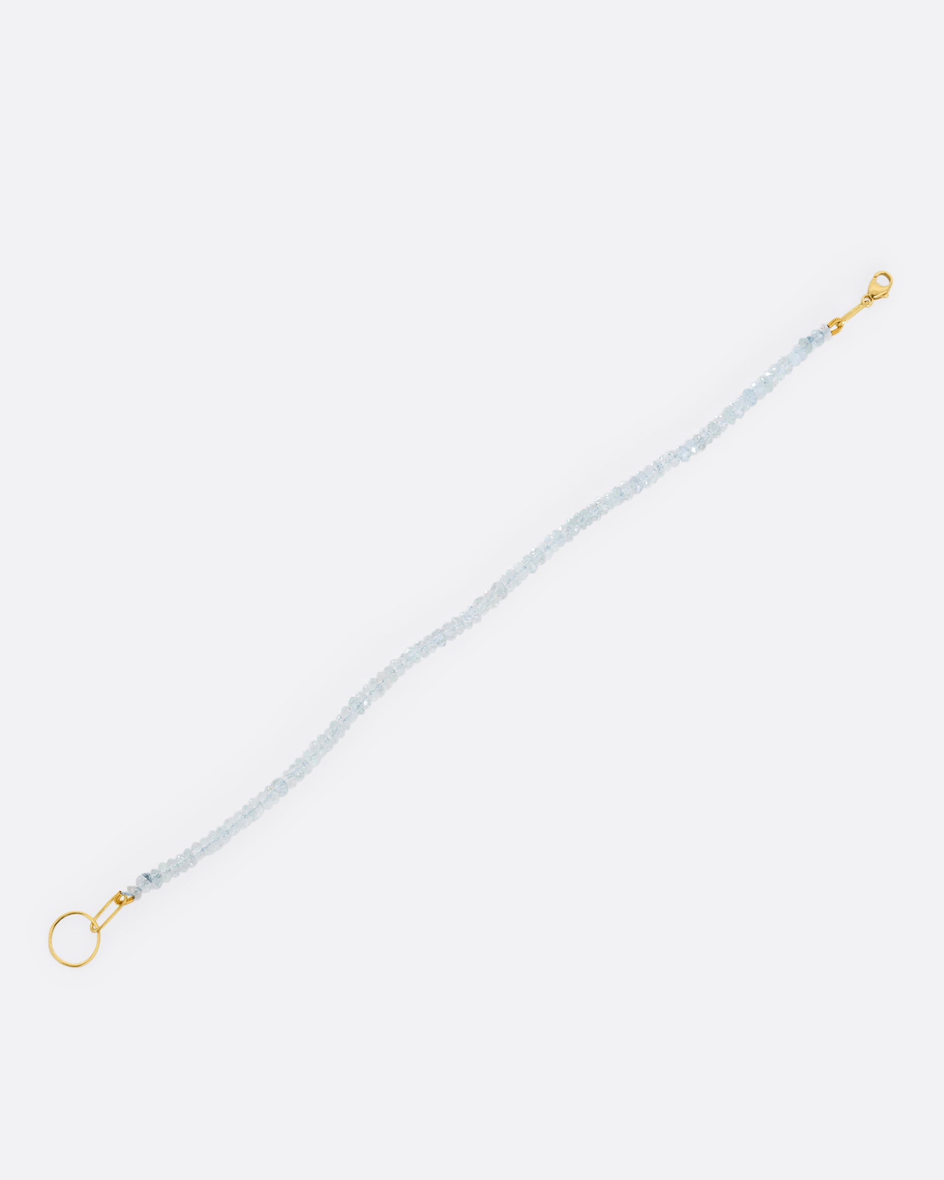A beaded aquamarine bracelet with a yellow gold clasp. Shown open lying diagonally flat from the top.