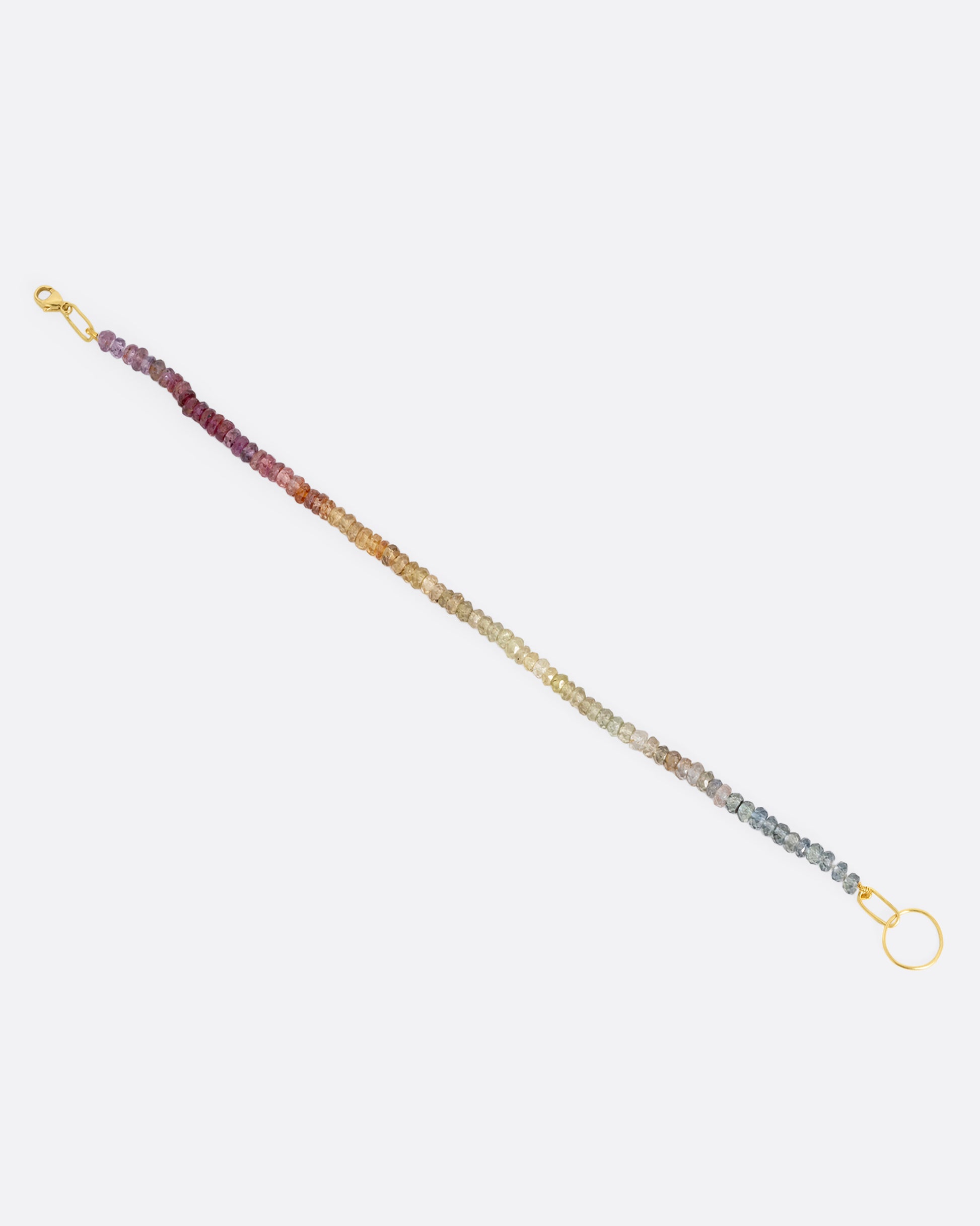 An ombré sapphire beaded bracelet with a yellow gold clasp. Shown open at a diagonal from the top.