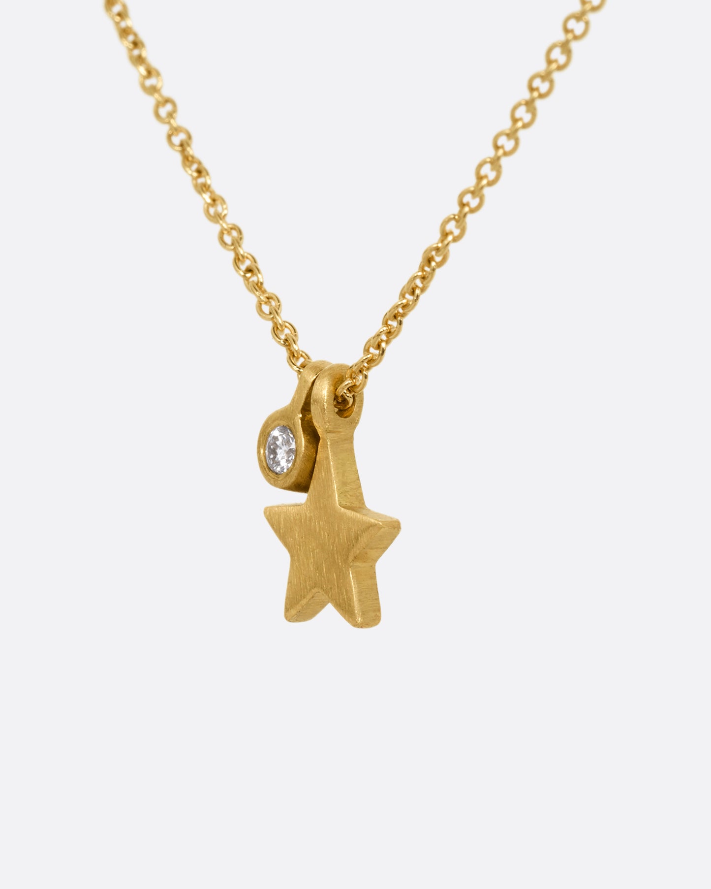 A yellow gold cable chain necklace with a tiny diamond tag and star charm. Shown from the side.
