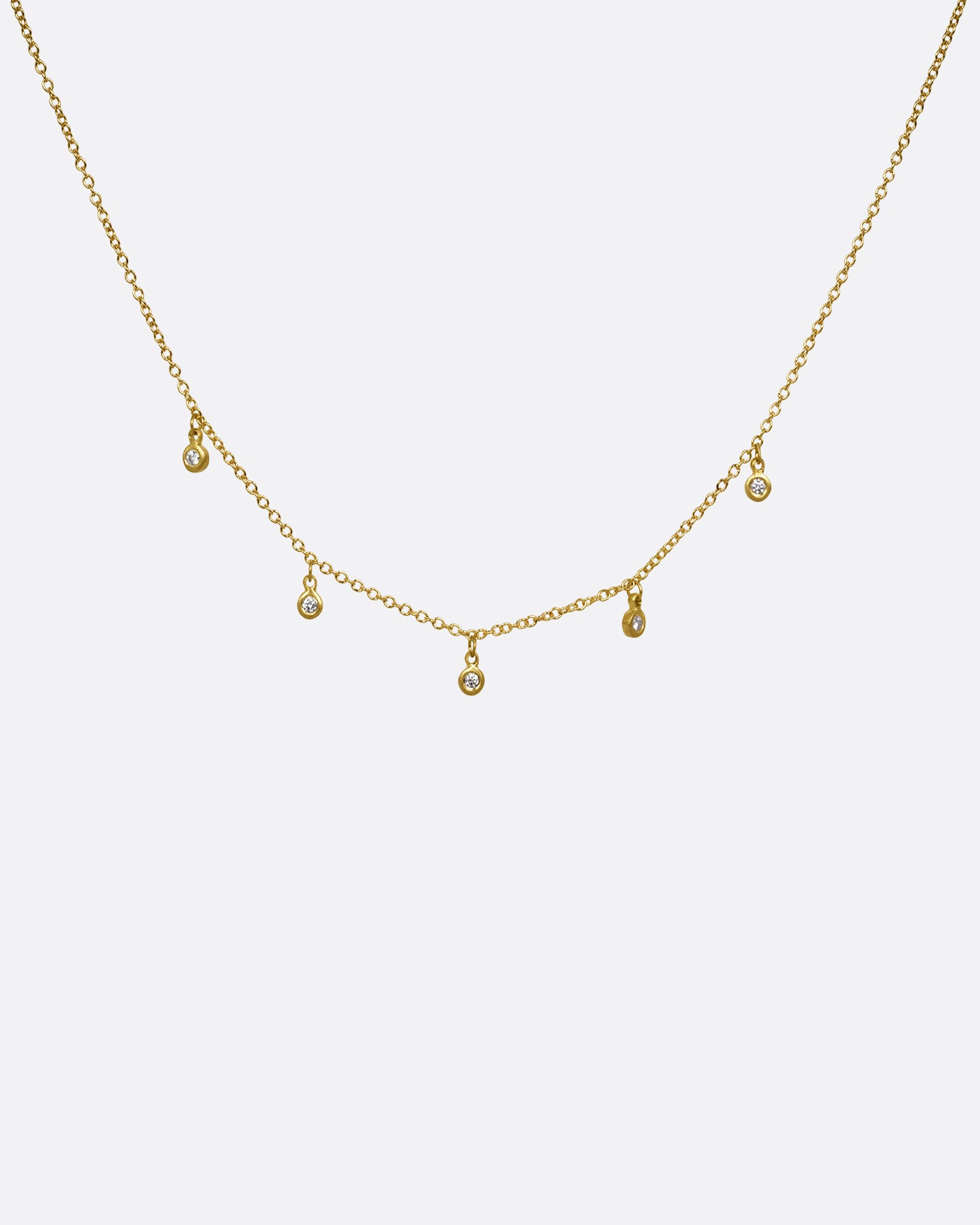 A yellow gold necklace with five brilliant bezel set diamond charms on a cable chain. Shown from the front.