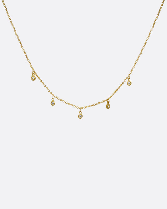 A yellow gold necklace with five brilliant bezel set diamond charms on a cable chain. Shown from the front.