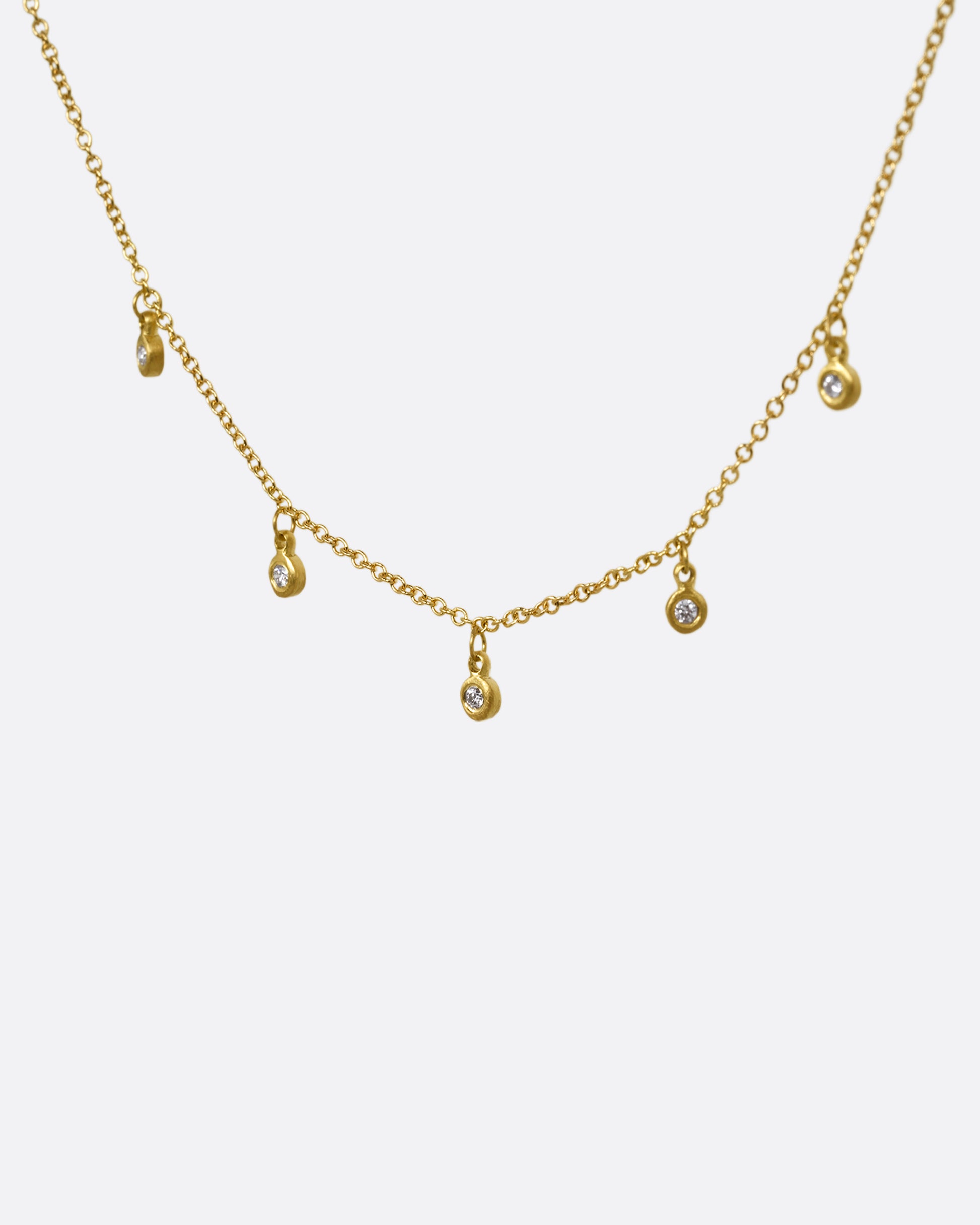 A yellow gold necklace with five brilliant bezel set diamond charms on a cable chain. Shown from the front.